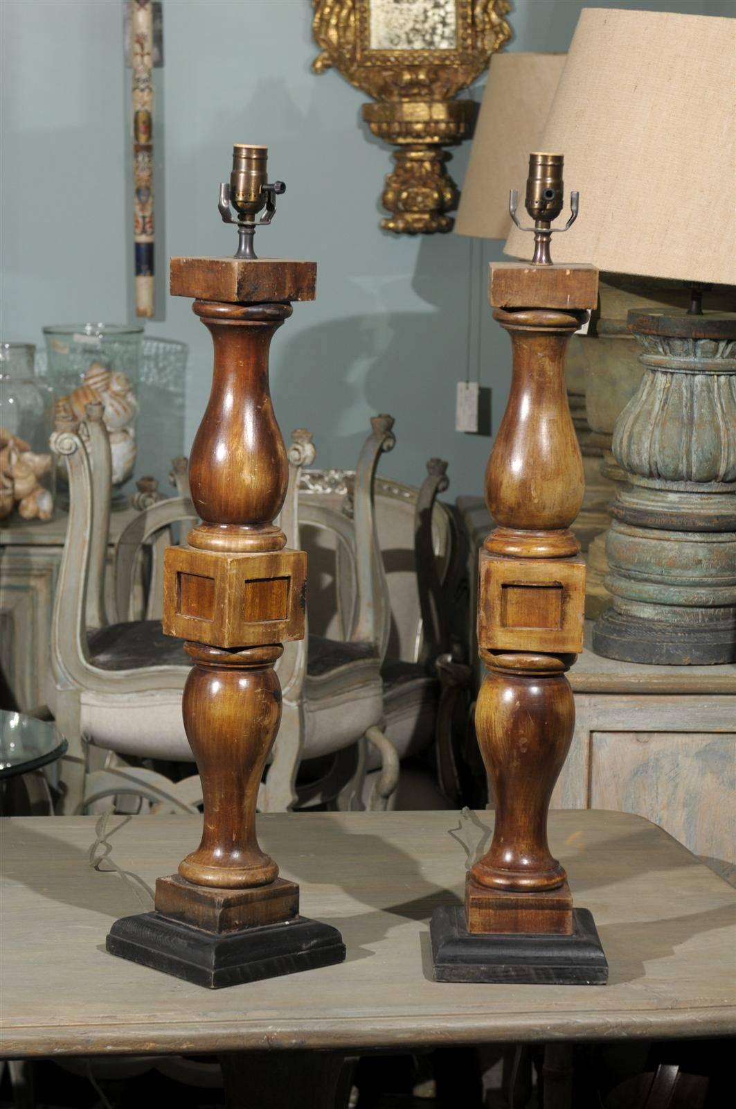 A pair of brown stained architectural turned wood banister table lamps. This pair of American table lamps from the 1920s is raised on a square black painted base. The pair is wired for the US market. The measurements provided (width and depth) are
