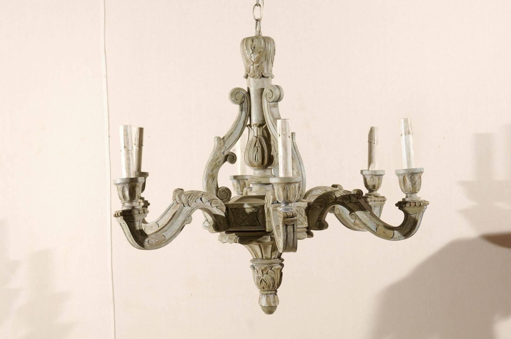 A French vintage six-light wooden chandelier. This French chandelier from the mid-20th century featured a central wooden column surrounded by carved volutes. Six scrolled arms support the wooden bobèches and painted candle sleeves. The wooden