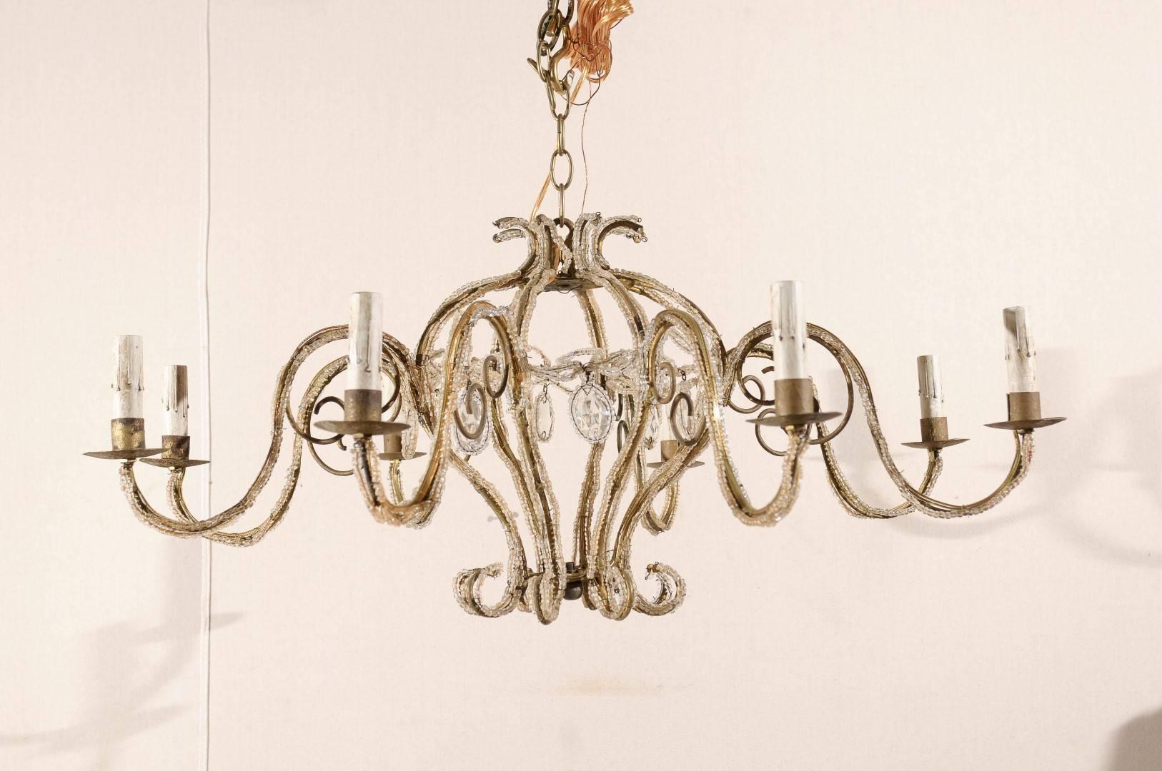 An Italian eight-light chandelier from the mid-20th century. This Italian chandelier features a central gilded armature made of S-scrolls from which delicate crystals and ribbon shaped beaded motifs hang. Eight swoop arms decorated with beading