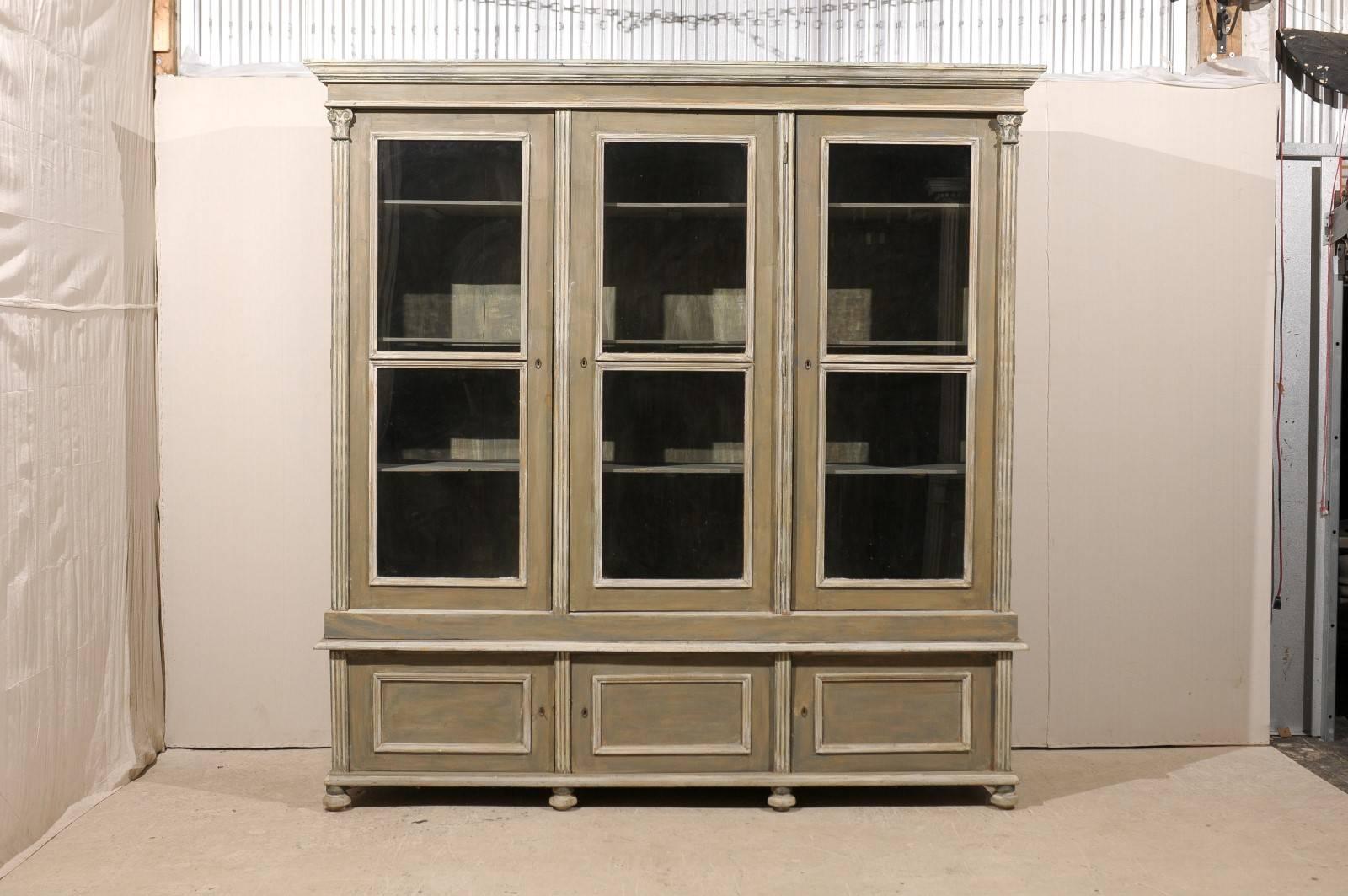 A 19th century French large glass door painted wood cabinet with three doors in the upper section and three smaller ones in the lower part. Flanked with thin columns. This French cabinet is raised on short round feet. The general color is of a green