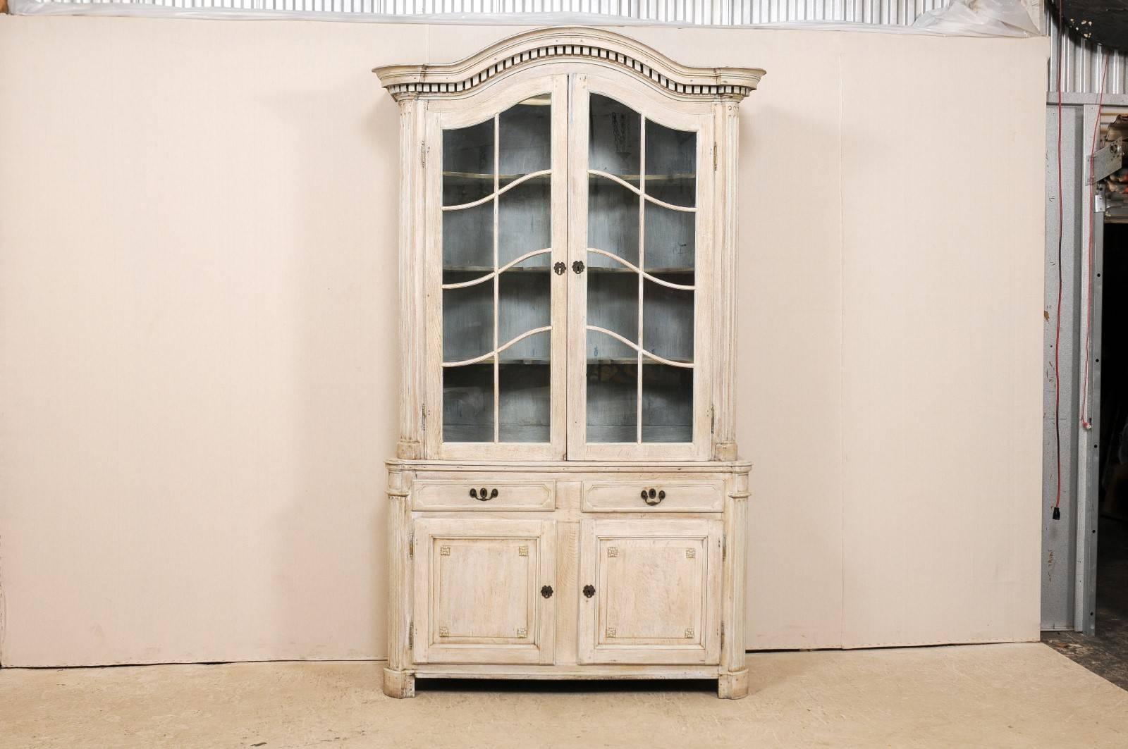 A mid-19th century French cabinet. This tall French cabinet has two upper glass front doors with shelves inside. The lower half of this cabinet has two drawers followed by two cabinet doors directly below. This piece features a bonnet type pediment