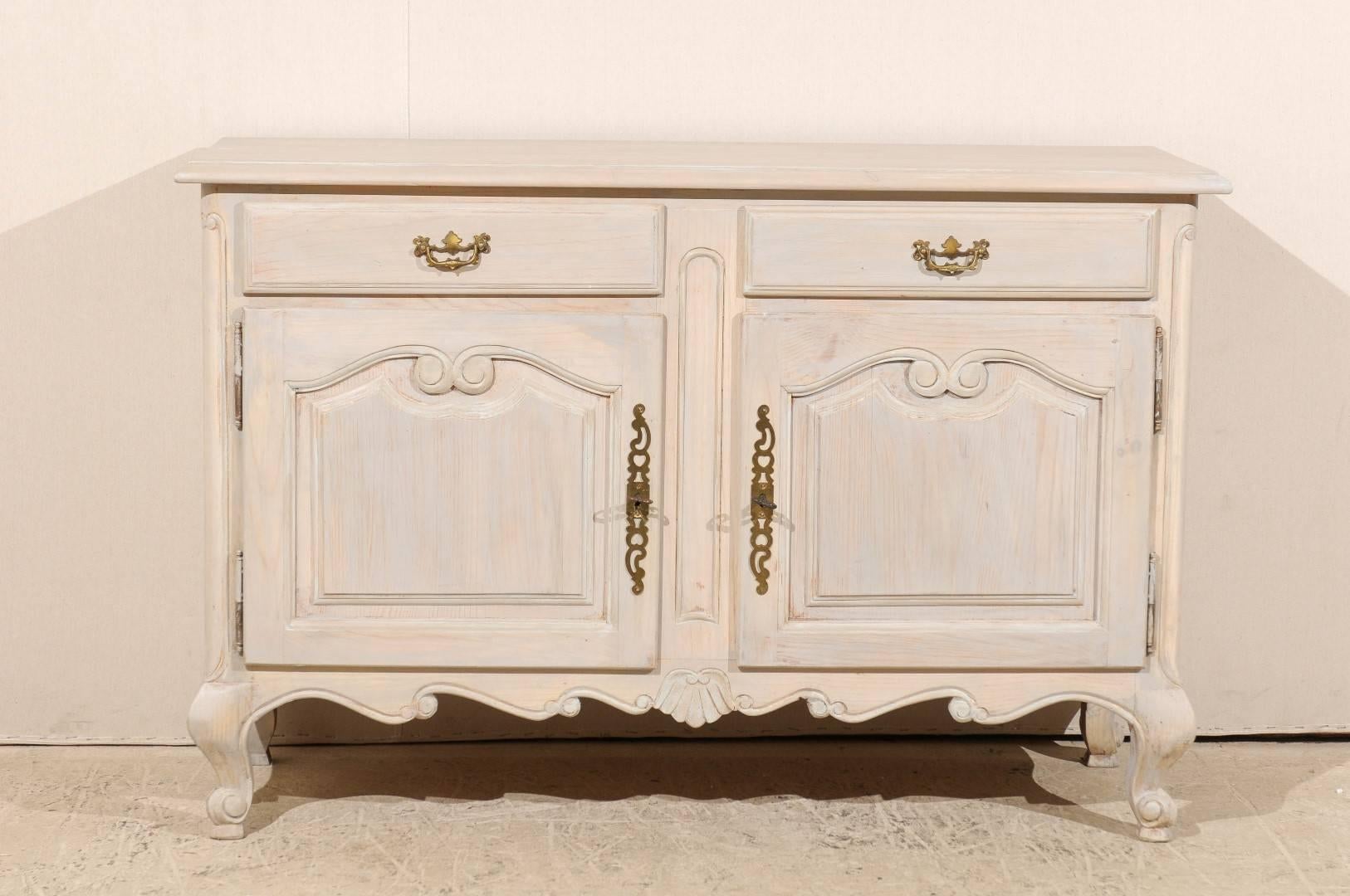 A French painted wood buffet. This vintage painted wood buffet features two drawers over two doors. The panels on the doors have been delicately carved. The skirt is scalloped with a shell motif in its center and the buffet is raised on scrolled