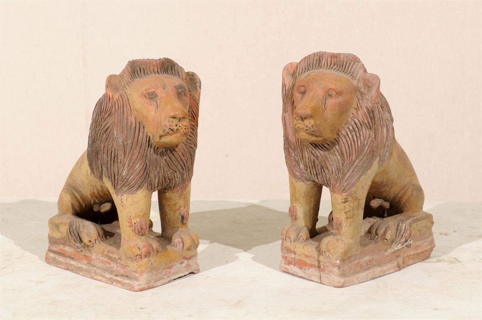 A pair of British colonial terracotta lions. This majestic pair of painted terracotta lions from the early 20th century will bring an air of regalness to any room.