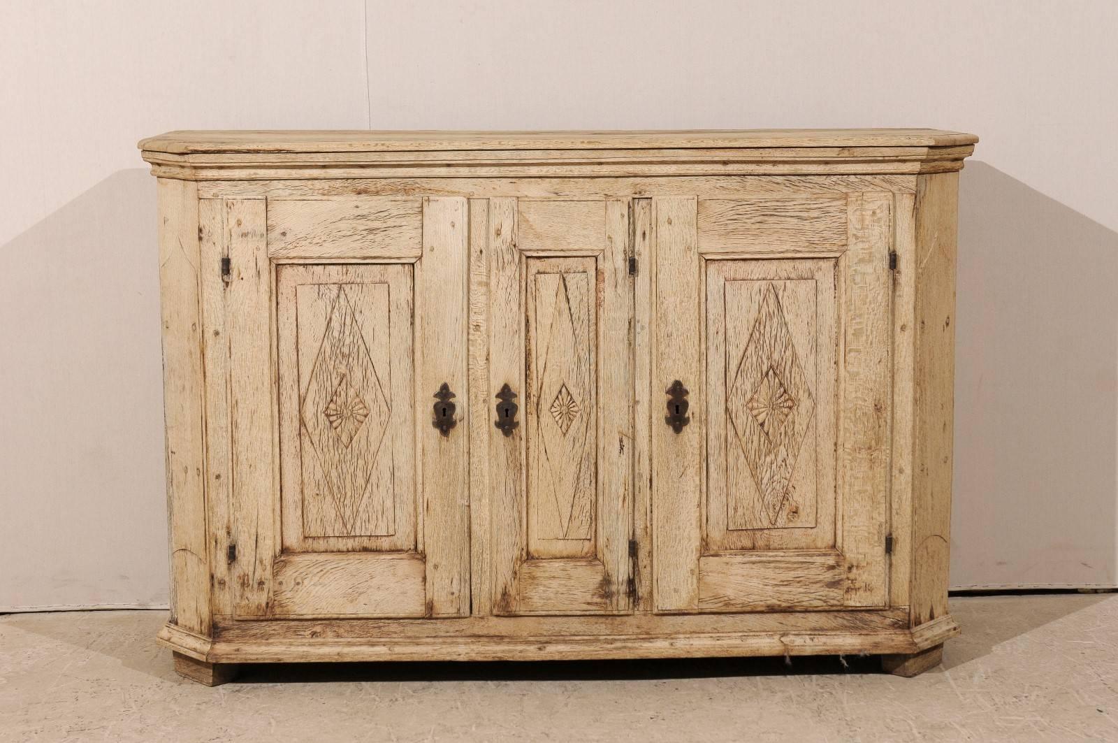 A French early 19th century sideboard. This French sideboard features three doors with diamond and floral carvings that open to interior shelves for great storage space. The side posts are canted. This piece has a natural pale wood finish. This