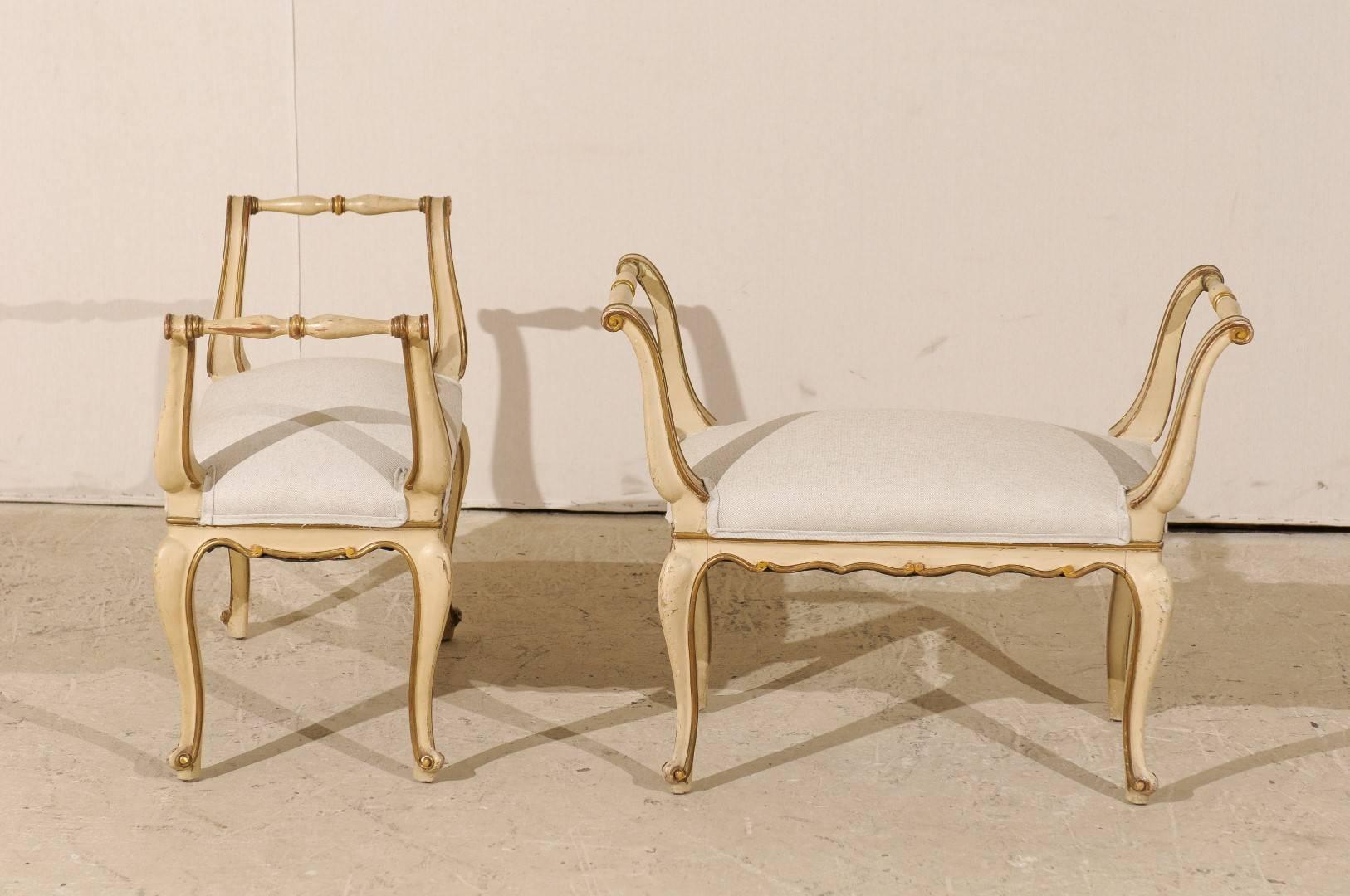 A pair of Italian vintage stools. These Italian mid-20th century wooden stools feature nice scrolled arms, cabriole legs, a nicely scalloped skirt and original paint made of beige, gold accents and brown trim. The stools have been newly upholstered
