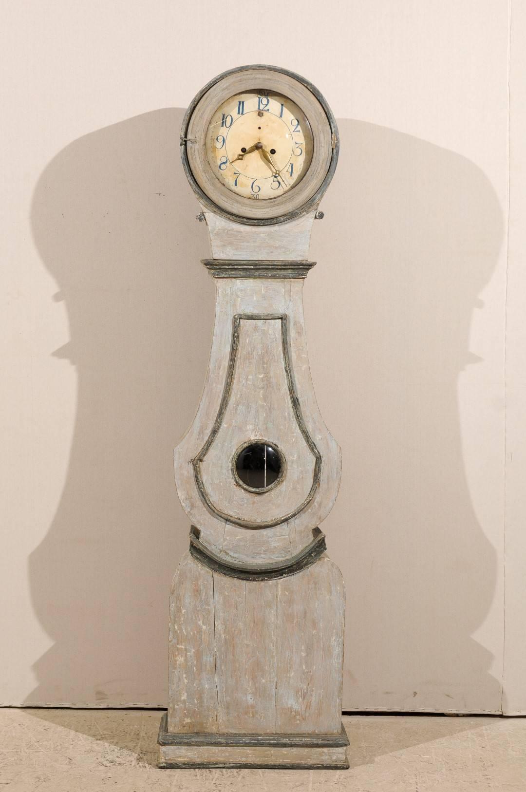 A 19th century Swedish clock commonly known as a Mora clock. This clock retains it's original metal face, hands and movement.  This clock is a very light blue-grey color with wood emerging through. The trim is a darker grey-blue color that stands