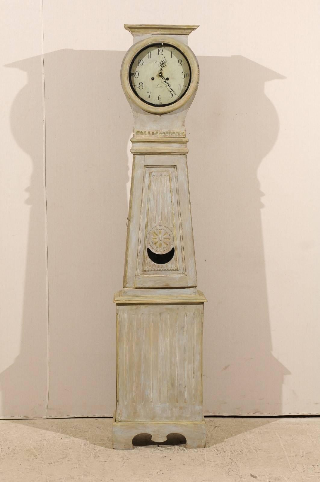 A Swedish painted wood clock from the 19th century. This Swedish clock from circa 1830-1840 features more of a linear shape compared to most of our clocks. Its round head is topped with a flat carving and a carved molding decorates the neck. The