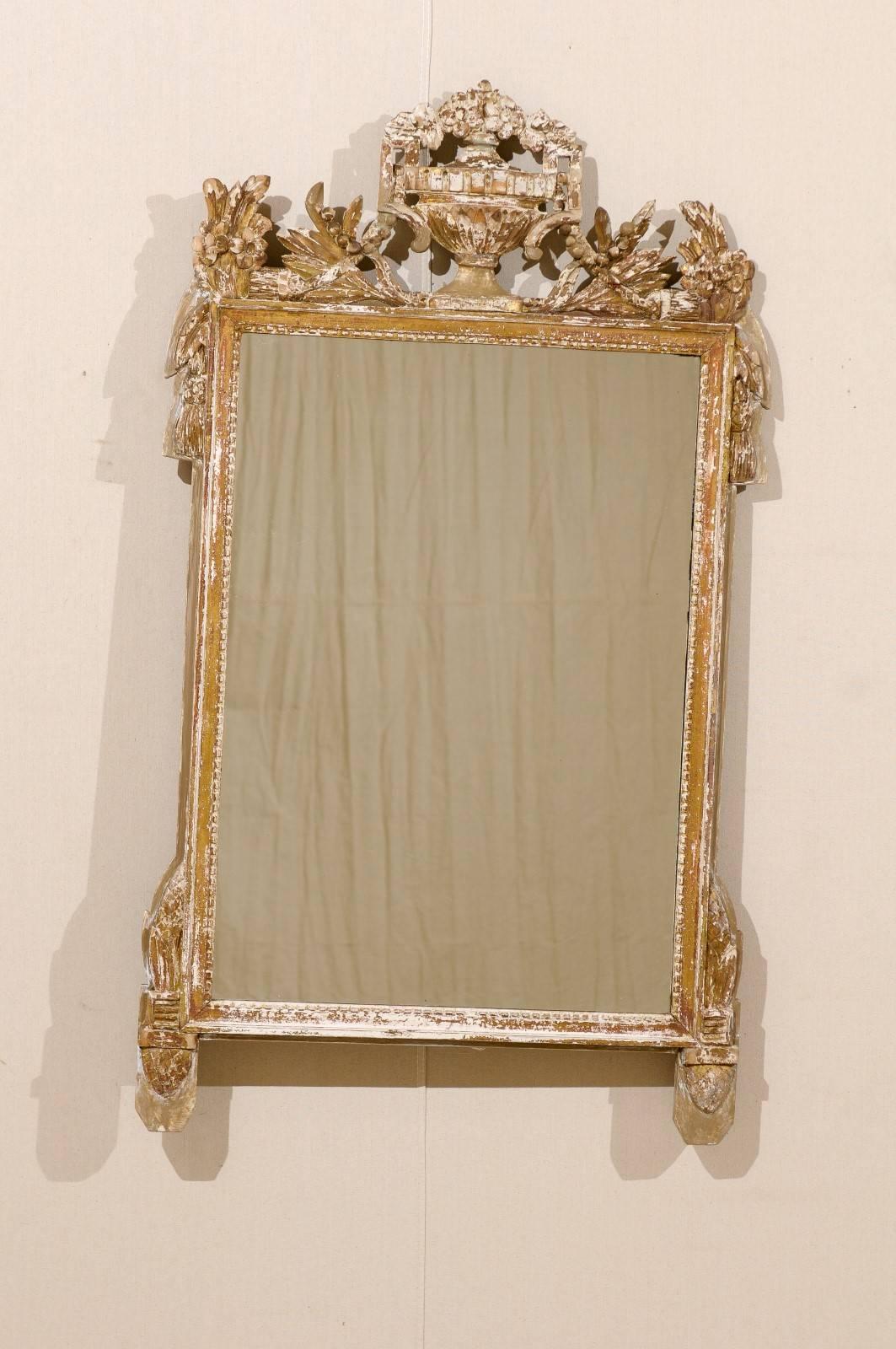 A French 19th century gilded wood carved mirror with nicely carved urn crest. This French, richly carved gilt mirror features an urn carving on the crest, accented by flowing floral and leaf motifs around it. It is gilded and also features a warm