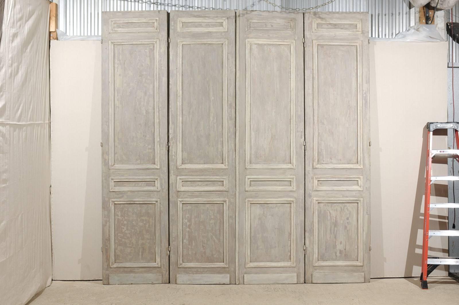 A set of French tall bi-folding doors from the 19th century. These two pairs of French bi-folding 10 feet doors have an overall green grey color tone with hints of blue. The doors are simply decorated with carved moldings of a darker green grey