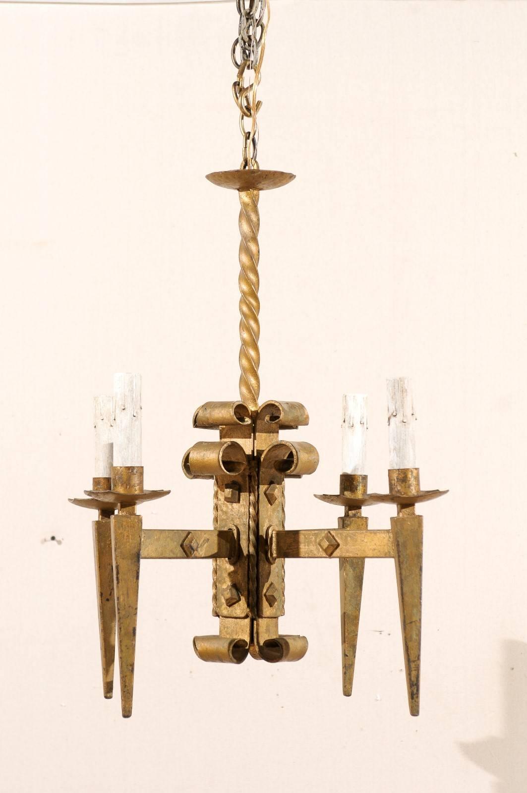 A French vintage gilded iron four-light chandelier. This French chandelier from the mid-20th century features a central beam from which four torch-shaped arms extend out to the metal bobeches and painted candle sleeves. The central beam and light