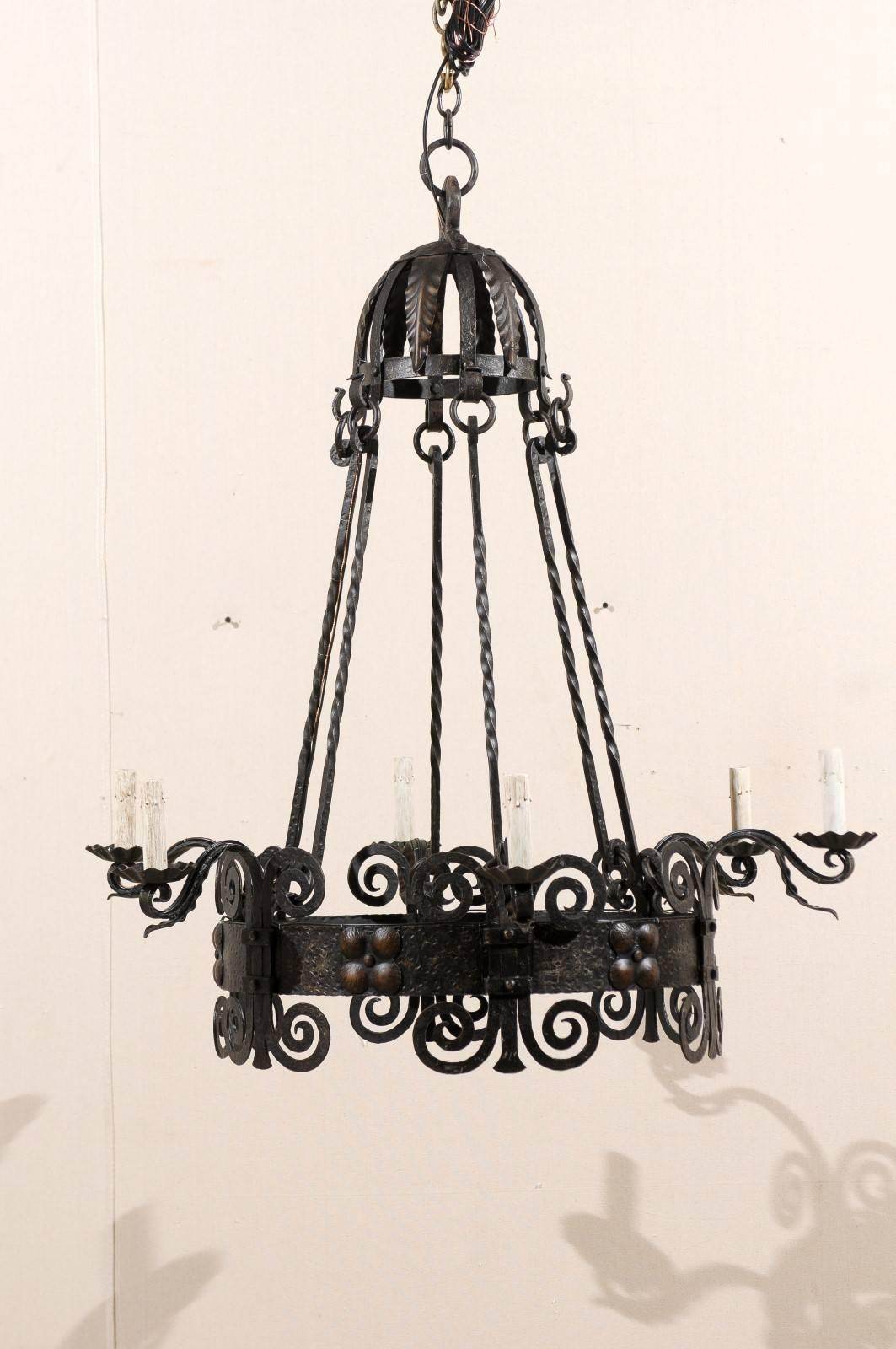 An Italian six-light black iron vintage chandelier. This mid-20th century Italian chandelier features scrolled motifs on the central circular ring with a raised, dotted flower design between each arm. This chandelier has the repeated scroll pattern