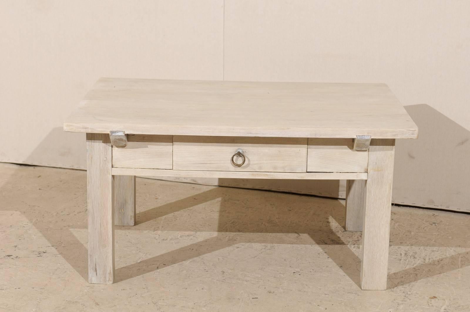 A Belgian wood coffee table with simple clean lines. This Belgian coffee table from the 1920s features a single drawer with a ring pull and straight legs. This coffee table with linear profile has a soft neutral cream color. This medium size piece