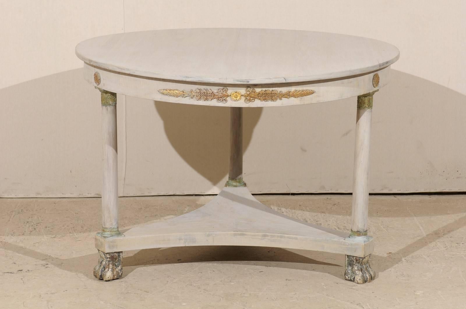A French 19th century round wood centre table. This French centre table of bleached mahogany has a round slightly warped top. This piece has a triangular stretchered shelf below which connects three legs. This table is raised on lion paw feet. Brass