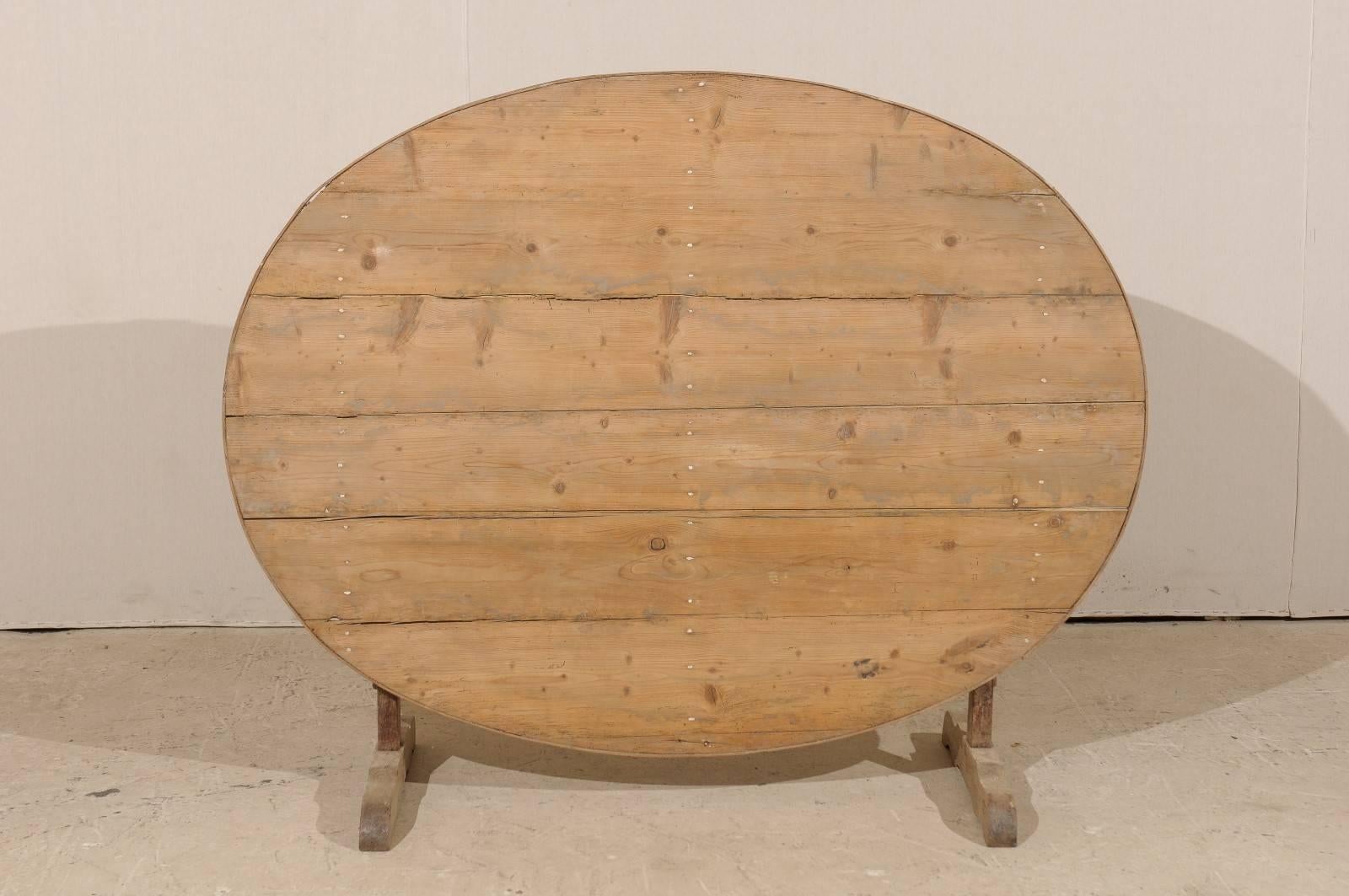 A French 19th century oval wine tasting table. This lovely rustic French wood table features a tilt top, which is the signature of wine tasting tables. This piece also features a butterfly wedge which turns to support the tabletop once the table is