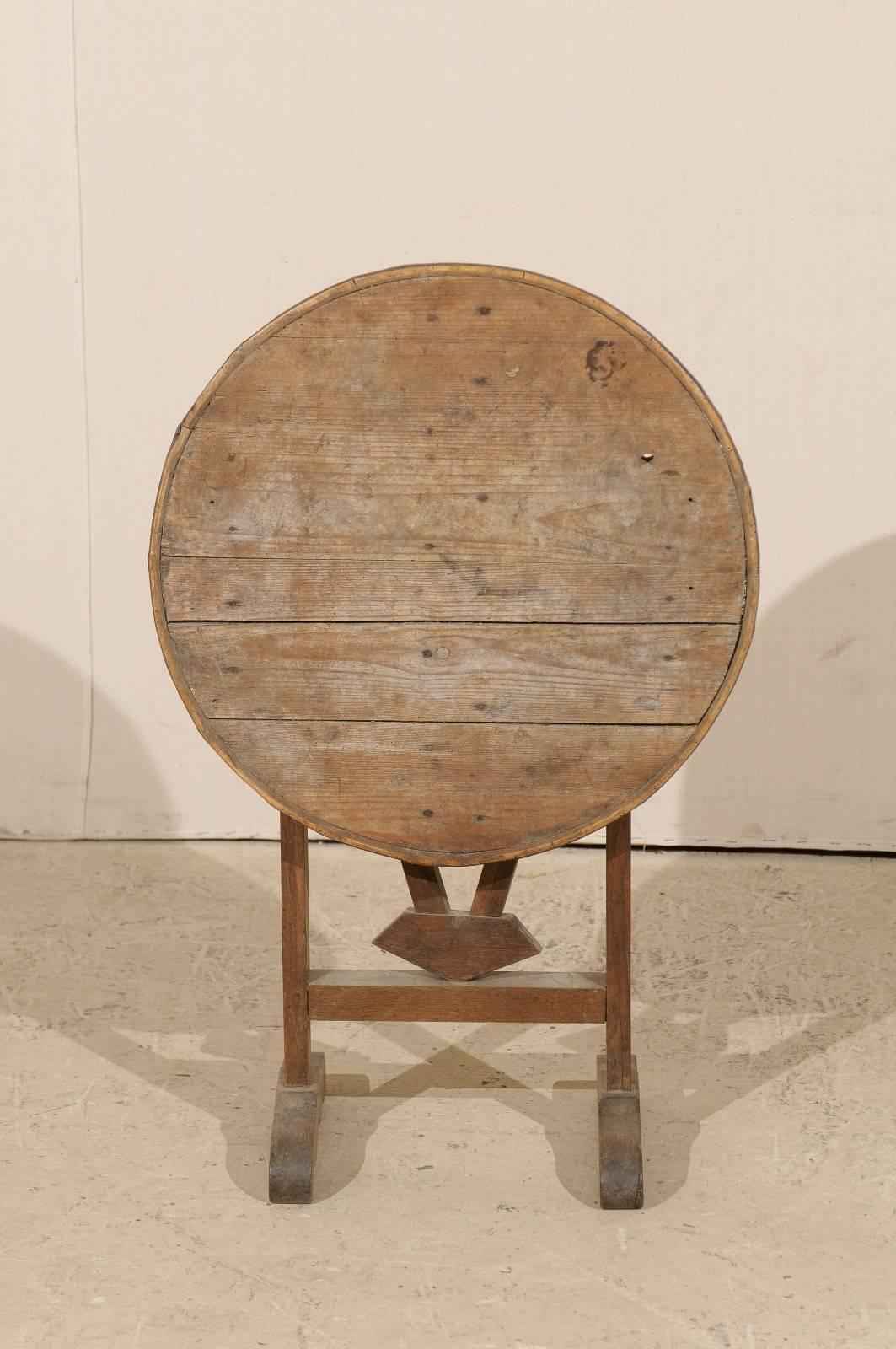 A petite sized French 19th century round wine tasting table. This rustic French wood table is unusually small and very cute! This table features a tilt-top, typical of wine tasting tables, along with a butterfly wedge which turns to support its top.