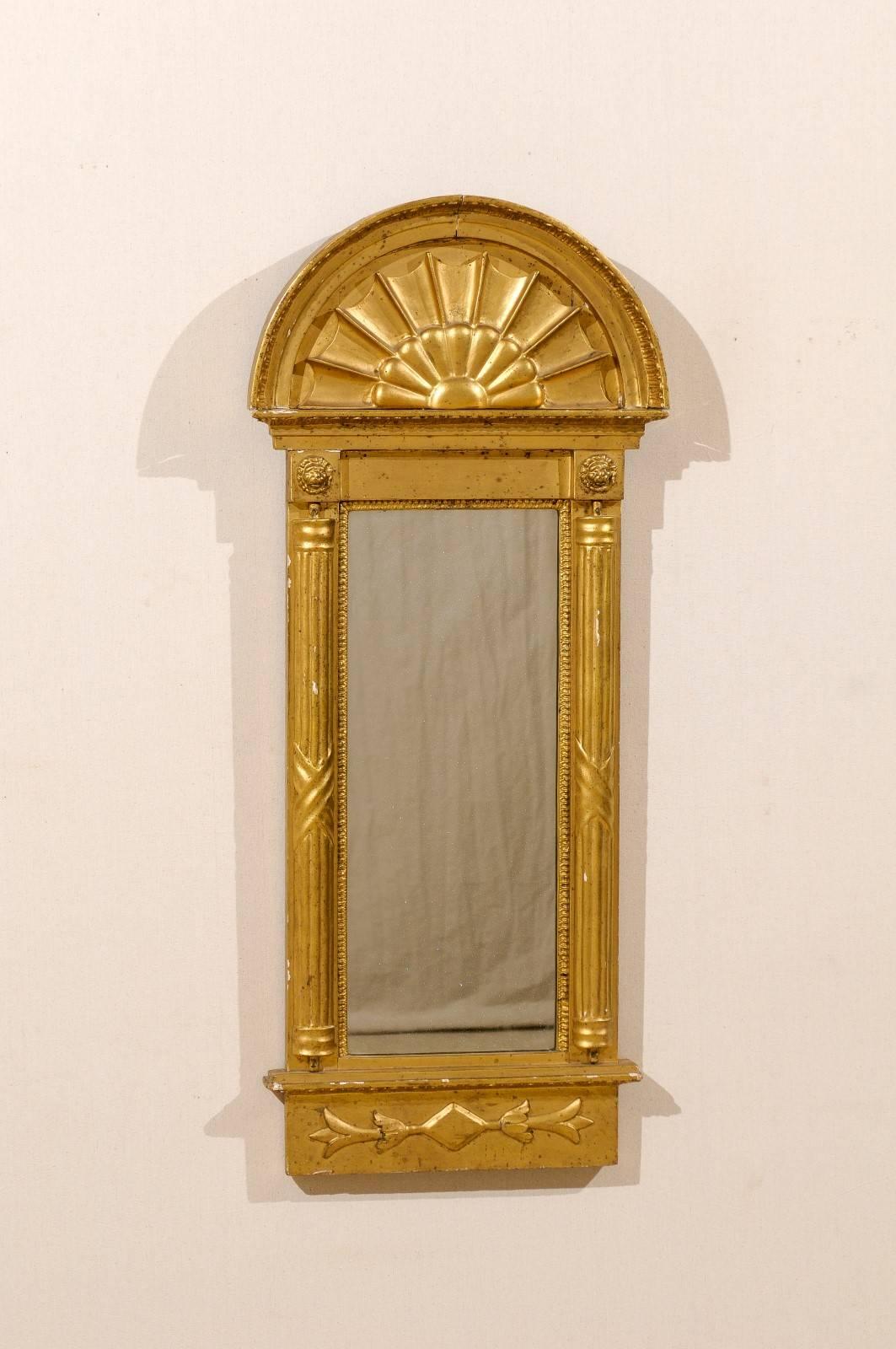 An early 19th century Swedish gilded mirror, circa 1820. This mirror features an arched crest and flanking fluted half columns. There are two lion carvings above each column. Within the arch there is a decoration reminiscent of a flower or a