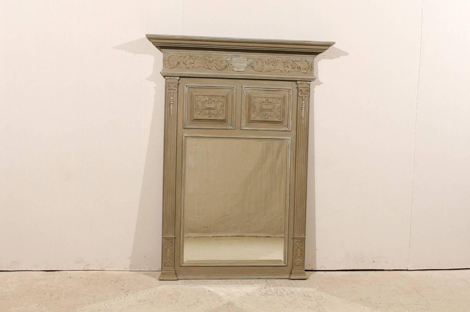 Miroir trumeau en bois peint et sculpté du début du XXe siècle. Ce miroir français présente des pilastres ioniques décorés d'un motif d'oves et de fléchettes au sommet de chaque colonne. Ce trumeau comporte également un récipient à fruits, une frise