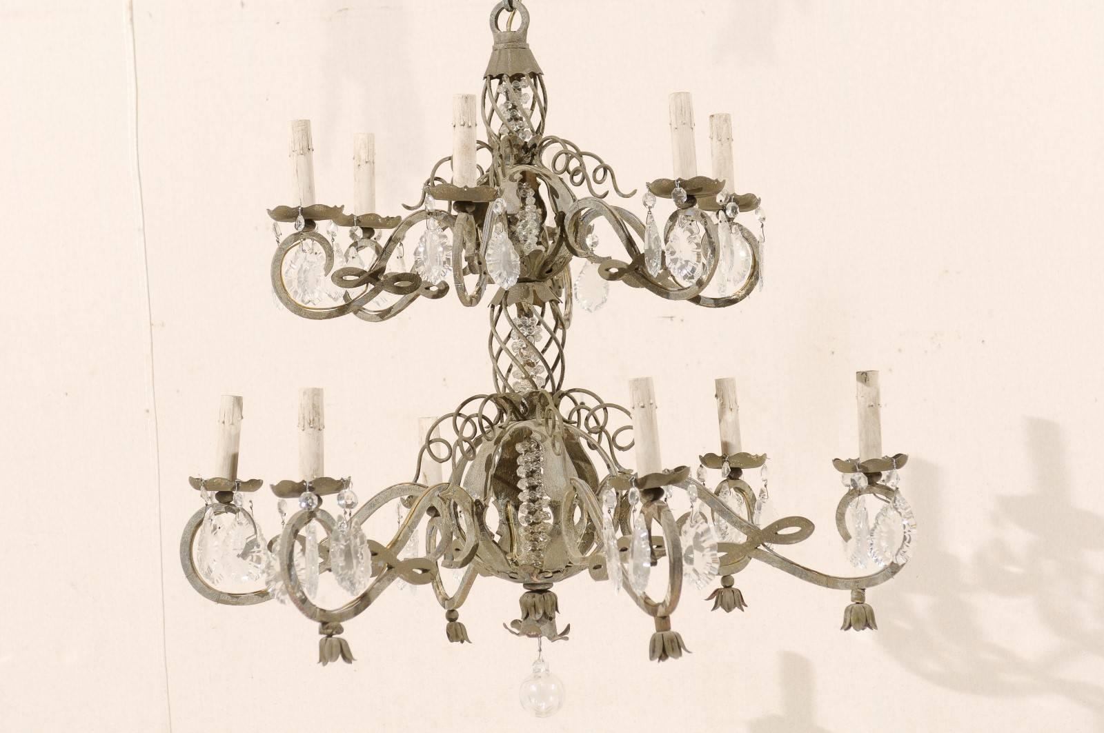 A French vintage two-tiered, twelve-light ornate metal and crystal chandelier. This lovely and intricate chandelier would look perfect in an entryway or hanging in a living room. It is adorned with features such as scrolled arms, decorative crystals