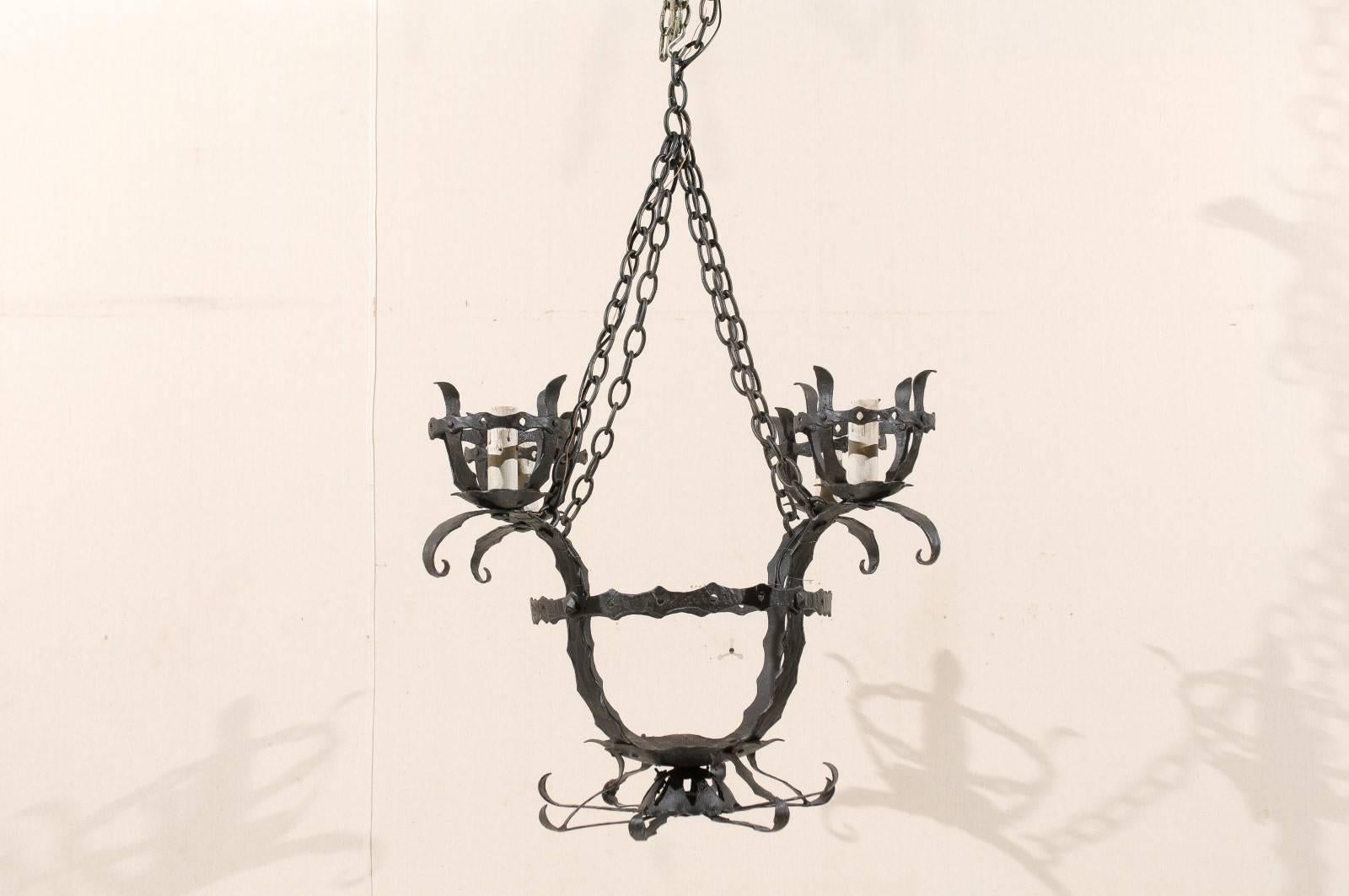 An Italian four-light iron chandelier. This Italian circular hammered iron chandelier from the mid-20th century features an overall basket style design. This piece has four arms that curve upward and support the repeated basket design four times