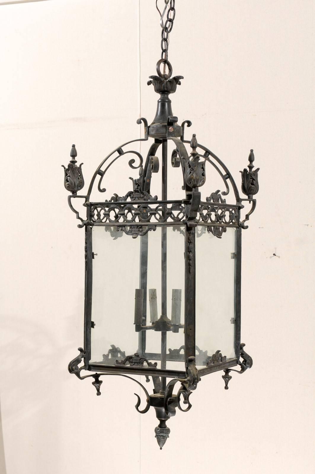A pair of large sized ornately decorated dark colored iron four-light English lanterns from the mid-20th century. Each lantern is decorated with a sprouting leaf motif at the top. Each one also features C-scroll motifs, acanthus leaf ornamentation