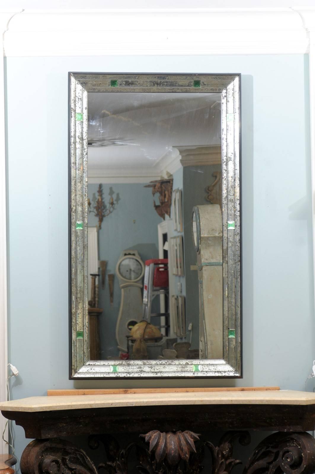 A rectangular mirror with small painted green églomisé square glass accents and antiquing throughout its border. This mirror also has a nice thin black frame around its edges. With the simplicity of its lines and discreet pop of the green colors,