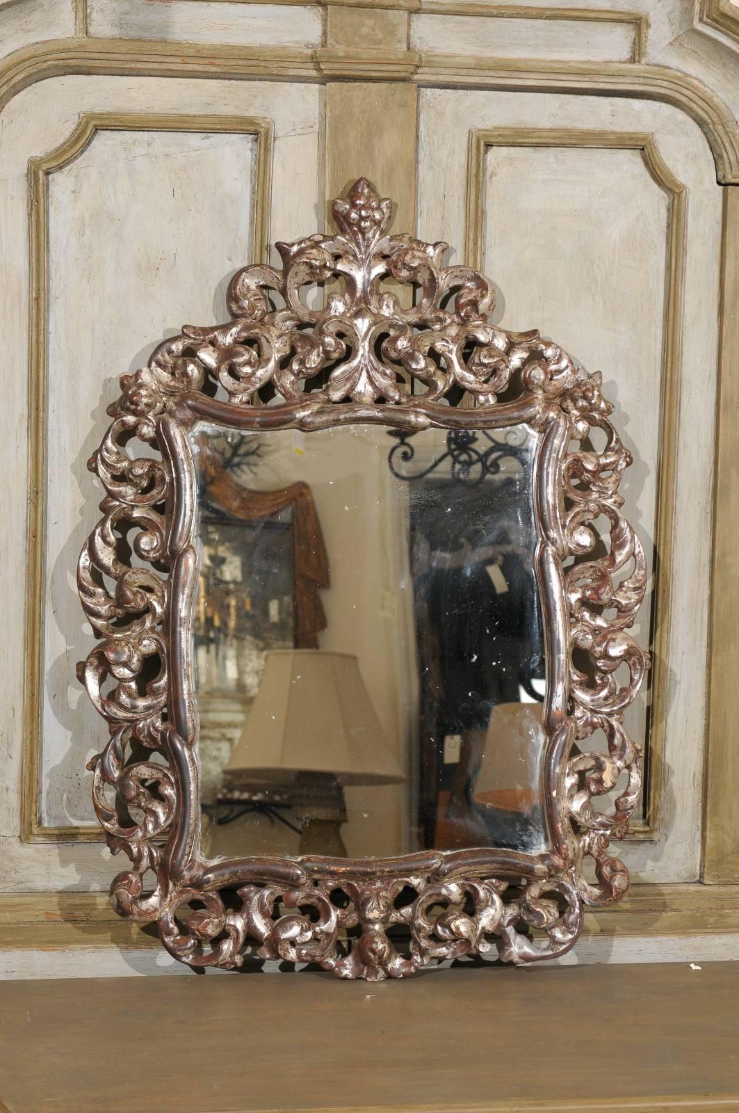 A beautifully carved Italian mirror from the early 20th century. This richly carved mirror is a warm bronze color with silver highlights throughout. This piece features ornate acanthus leafs and scrolls in the surround. At the crest of this piece