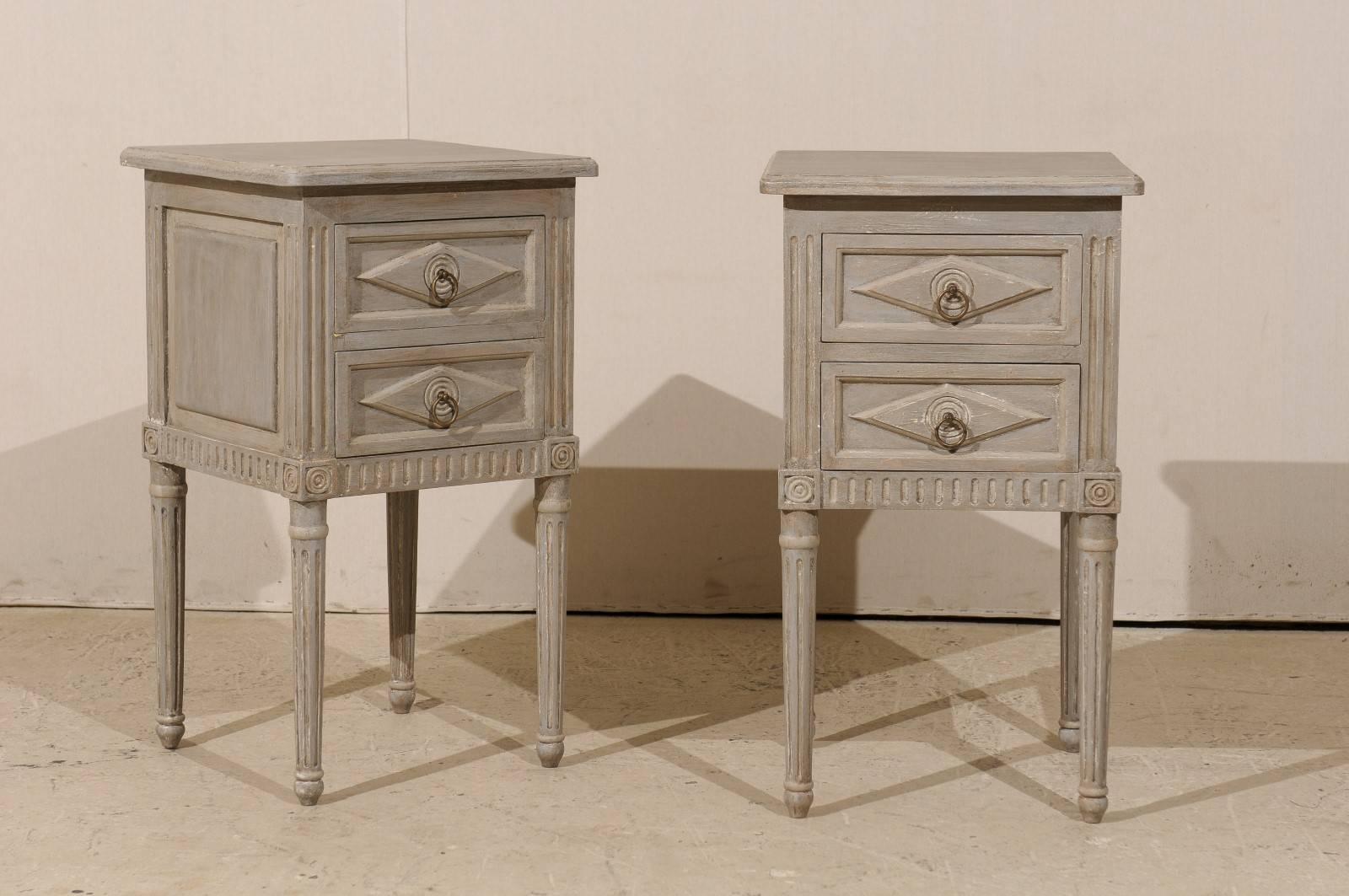 A pair of small size two-drawer painted wood nightstand tables or chests. These small size chests feature a carved horizontal diamond inset onto the drawers. The decor is elegant yet discreet, with fluted motifs flanking the drawers, as well as