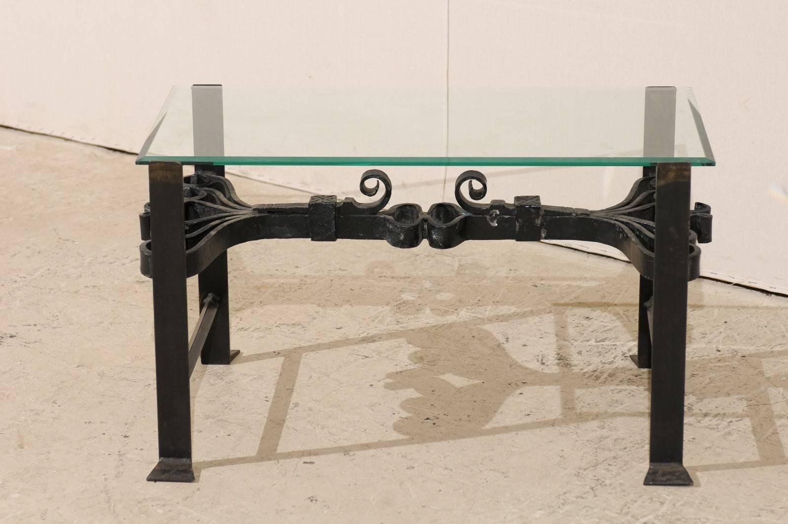 A wrought iron coffee table with glass top. This rectangular shaped coffee table features 19th century Italian fragments used to make the very intricate cross stretcher. The ornately scrolled motifs connect the newer simple and linear legs. This