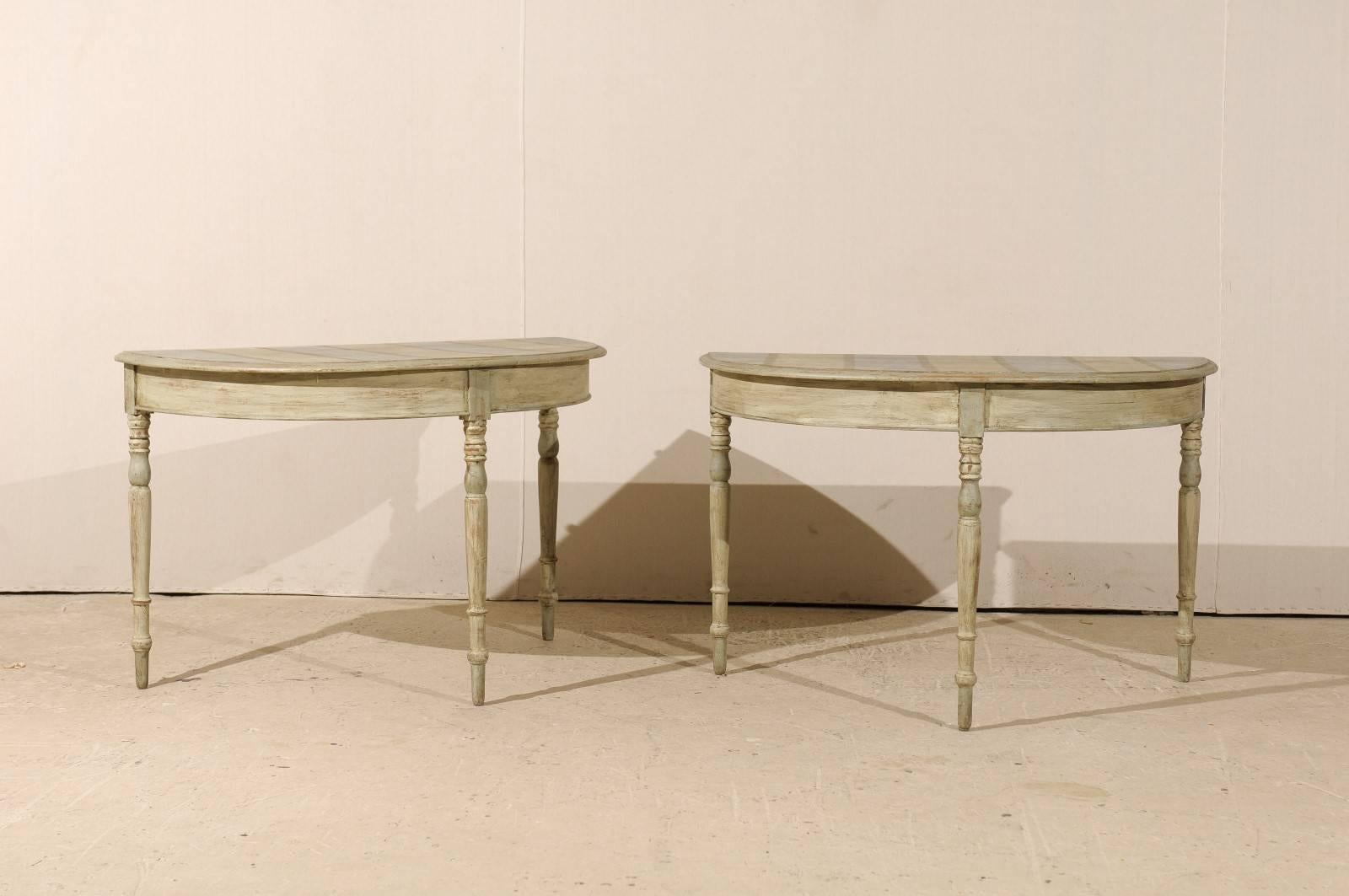 A pair of 19th century Swedish demilune tables. This pair of painted wood demilune tables features half moon tops over round aprons. These demilune console tables are raised on three turned and tapered legs. The tops consist of a wide stripe pattern