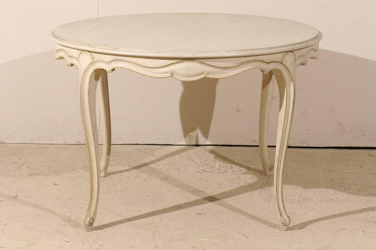 A French Louis XV style round top centre table. This French vintage painted wood table from the mid-20th century has a delicately carved and scalloped apron with gilded motif in the surround and along the four cabriole legs. This French Louis XV