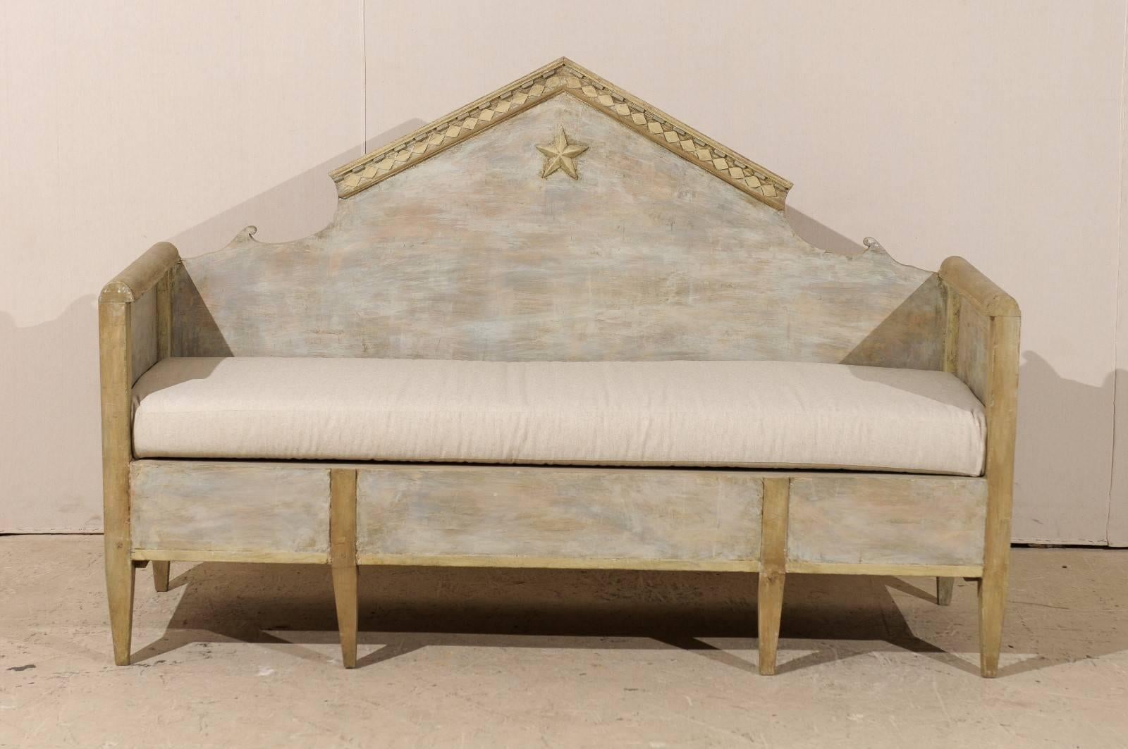 A Swedish Karl Johan style bench from the early 1800s. This 19th century Swedish painted wood sofa bench features a pyramidal back pediment with a five-pointed star at the top center, high arms and tapered legs. The overall color of this piece is a