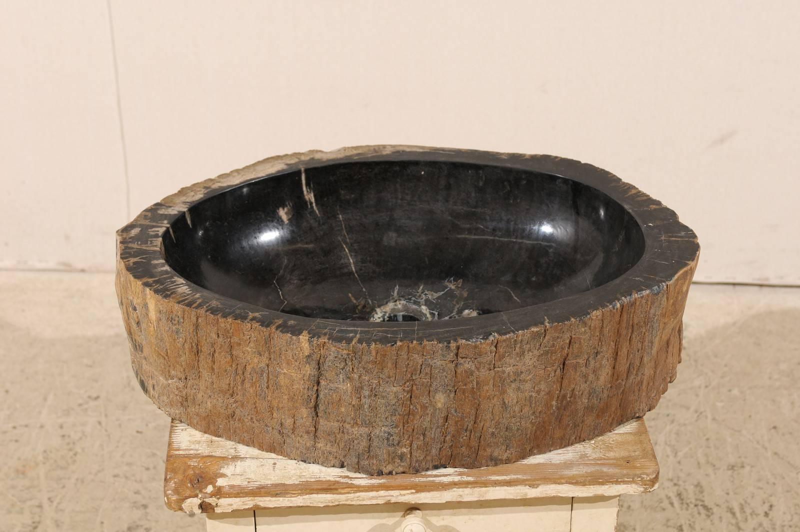 A black petrified wood sink. This petrified wood sink features a round shape. The inner part of the sink is black in color with lighter veins and has been polished. The surround has been left unpolished. The sink has been drilled for US plumbing and