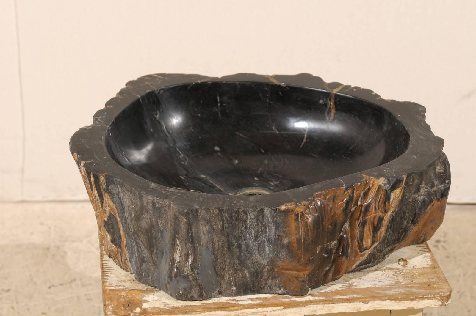 An exquisite black petrified wood sink. This petrified wood sink features an uneven round shape. The bowl is primarily black and polished while the exterior is unpolished and black and brown in color. This sink has been drilled for US plumbing and