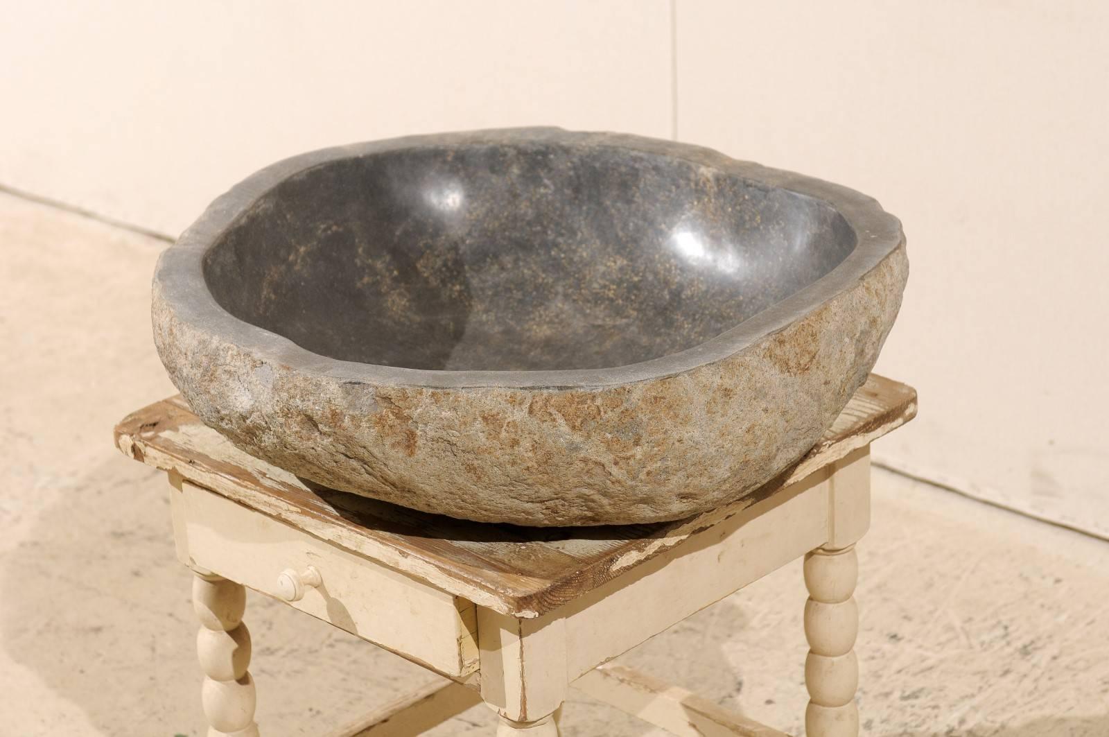 A river rock sink carved from a natural river rock boulder. This sink has a polished bowl with natural stone on the exterior. It is mostly a light grey color and tan on the outside and is more of a black tone towards the center. This piece would be