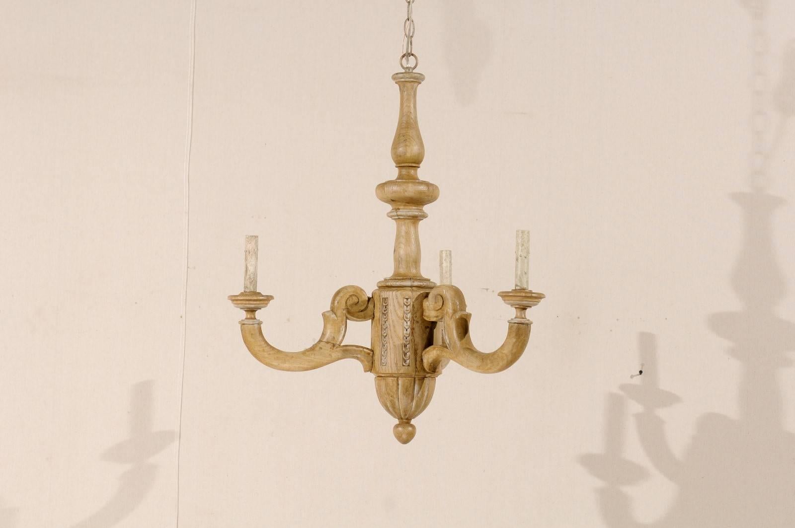 A French three-light carved wood chandelier. This French chandelier from the mid-20th century has a natural wood finish and features a central column with three arms extending out from geometrical volutes into a soft swoop and up to the bobèches.