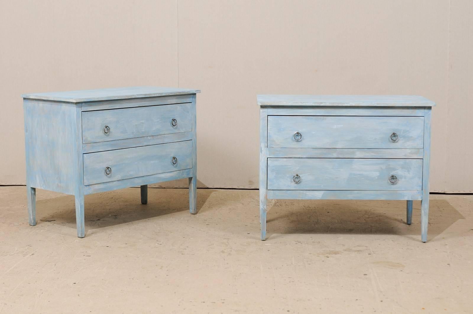 A pair of American painted wood chests. This pair of American two-drawer chests from the 20th century feature nice clean lines and drawers which are minimally ornamented with ring pulls. The chests are raised on slightly tapered legs. This pair of