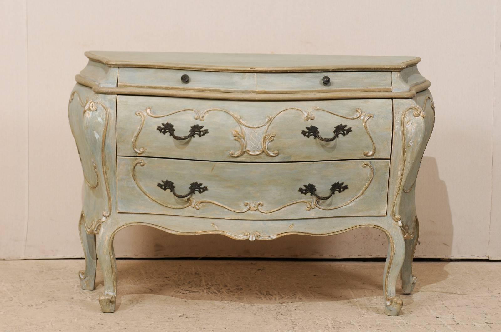 An American Bombé style painted wood chest. This American Bombé chest from the late 20th century is ornately decorated with a shell carving on the skirt and cartouche outline around the drawers and chest sides. This Bombay style chest features two