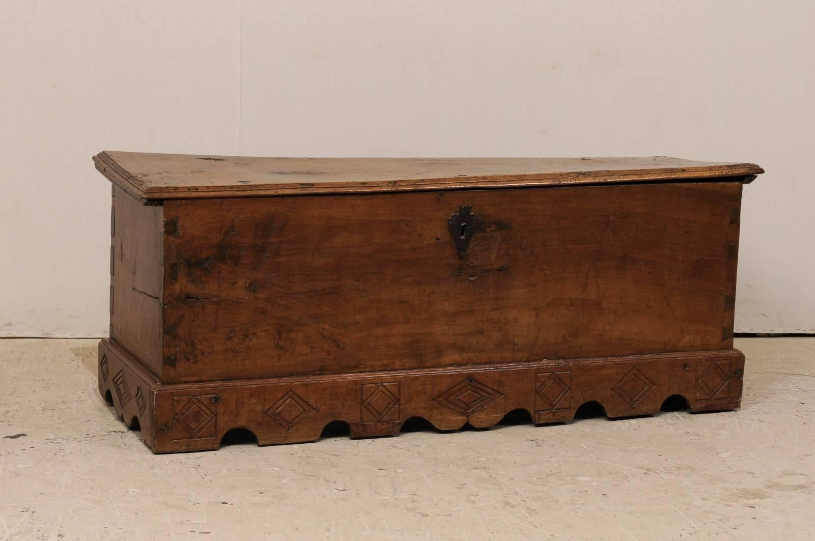 A Spanish 18th century large size wood coffer. This Spanish trunk from the 18th century features beautifully visible dovetail joints down each corner side and a scalloped skirt which is adorned with geometrical carvings. The trunk's interior offers