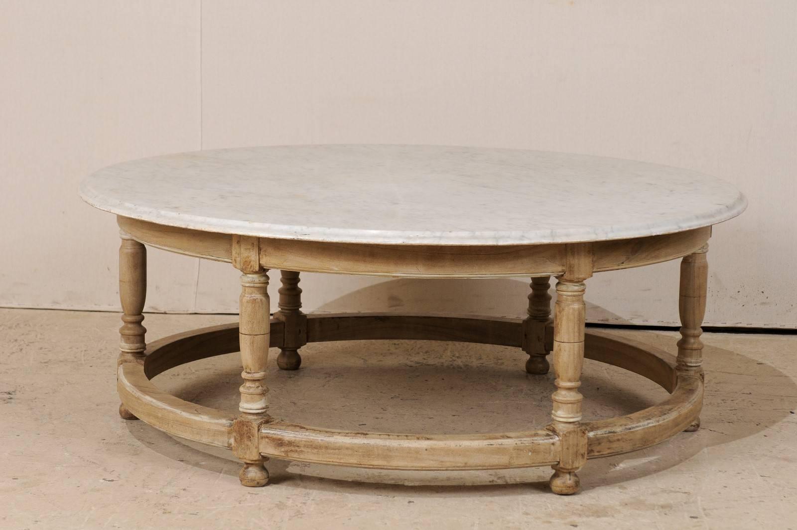 A French mid-20th century oversized round marble top coffee table. This French Mid-Century coffee table has a white marble top with black and grey veining throughout. The base is circular in shape with turned legs and curved apron and stretchers.