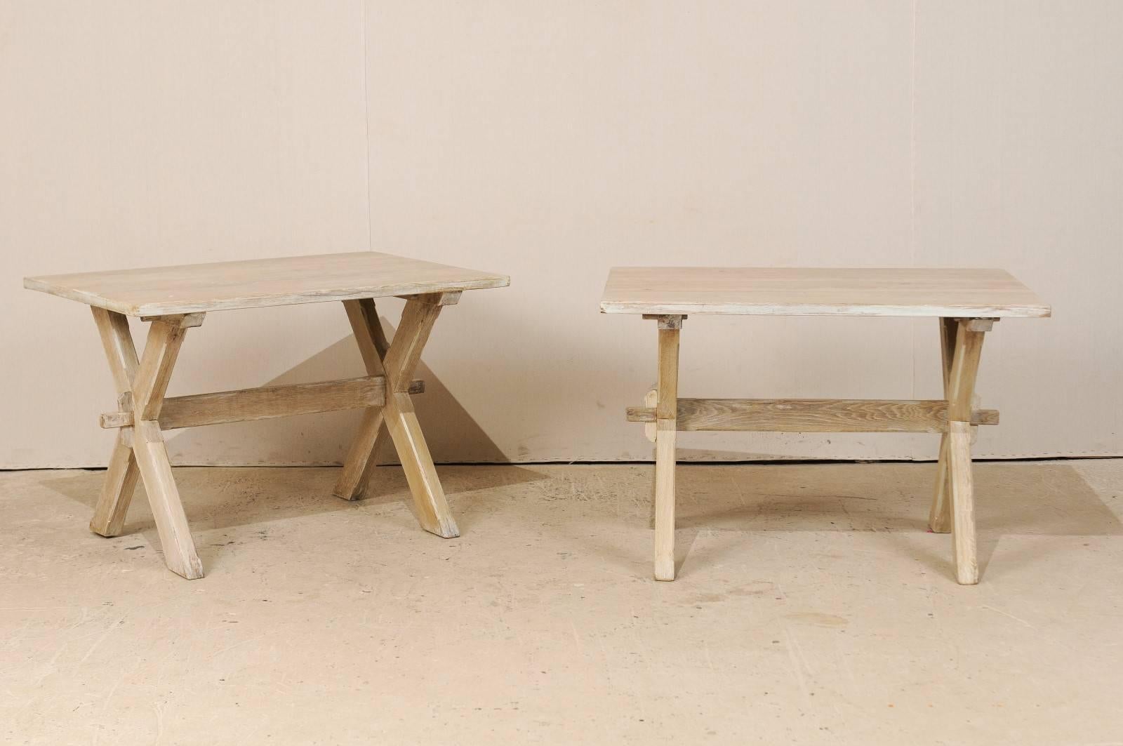 A pair of French Mid-Century side or accent tables. This pair of French wood tables features clean simple lines with the crossed or X-style legs. The tables from the mid-20th century are a natural finish with lighter cream accent trim paint. This