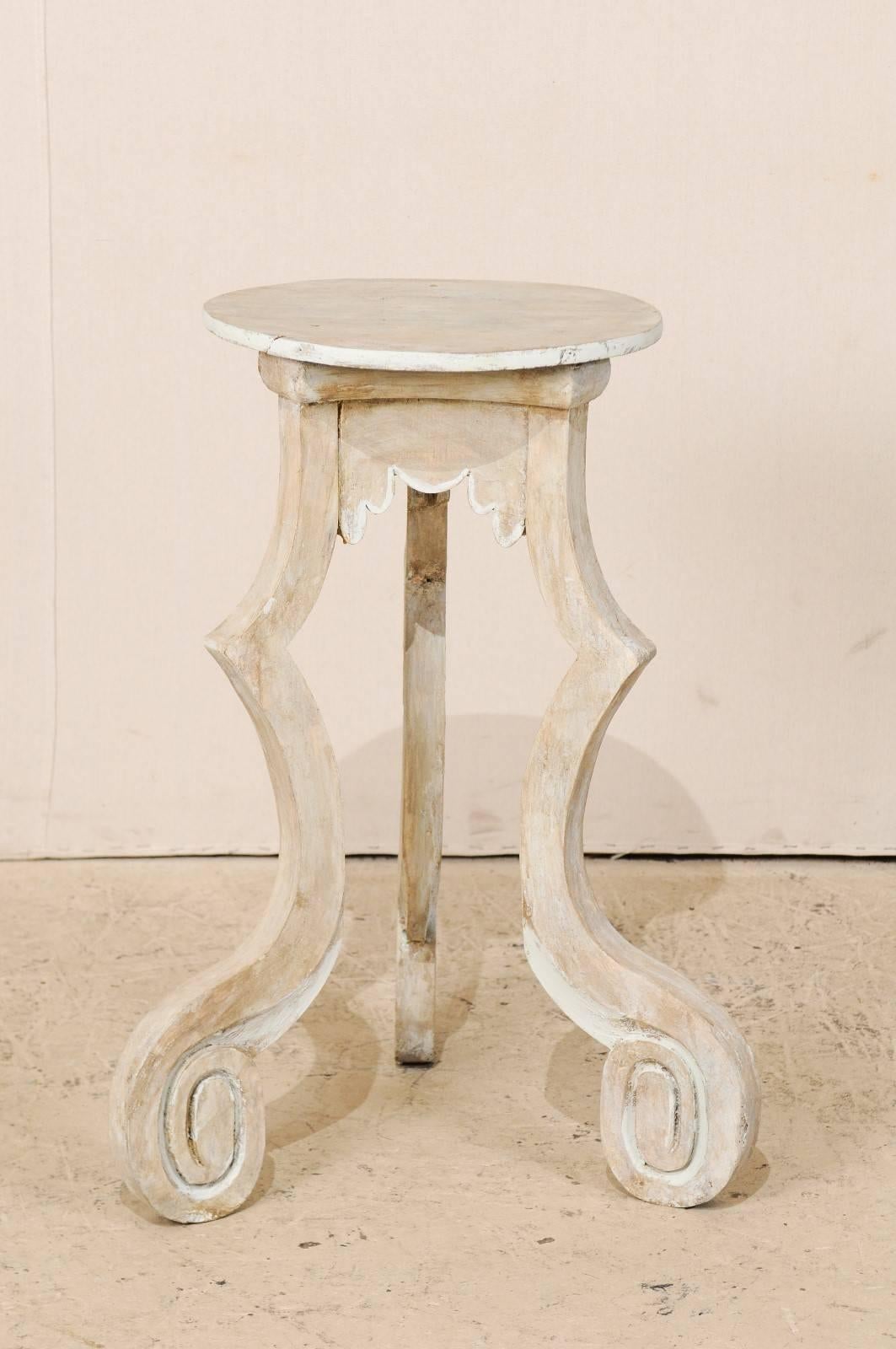 A Spanish light colored painted wood table stand. This relatively small Spanish table from the early 20th century is sure to add a bit of whimsy to any room! This table has a round shaped top and scalloped skirt. There are three quirky legs which