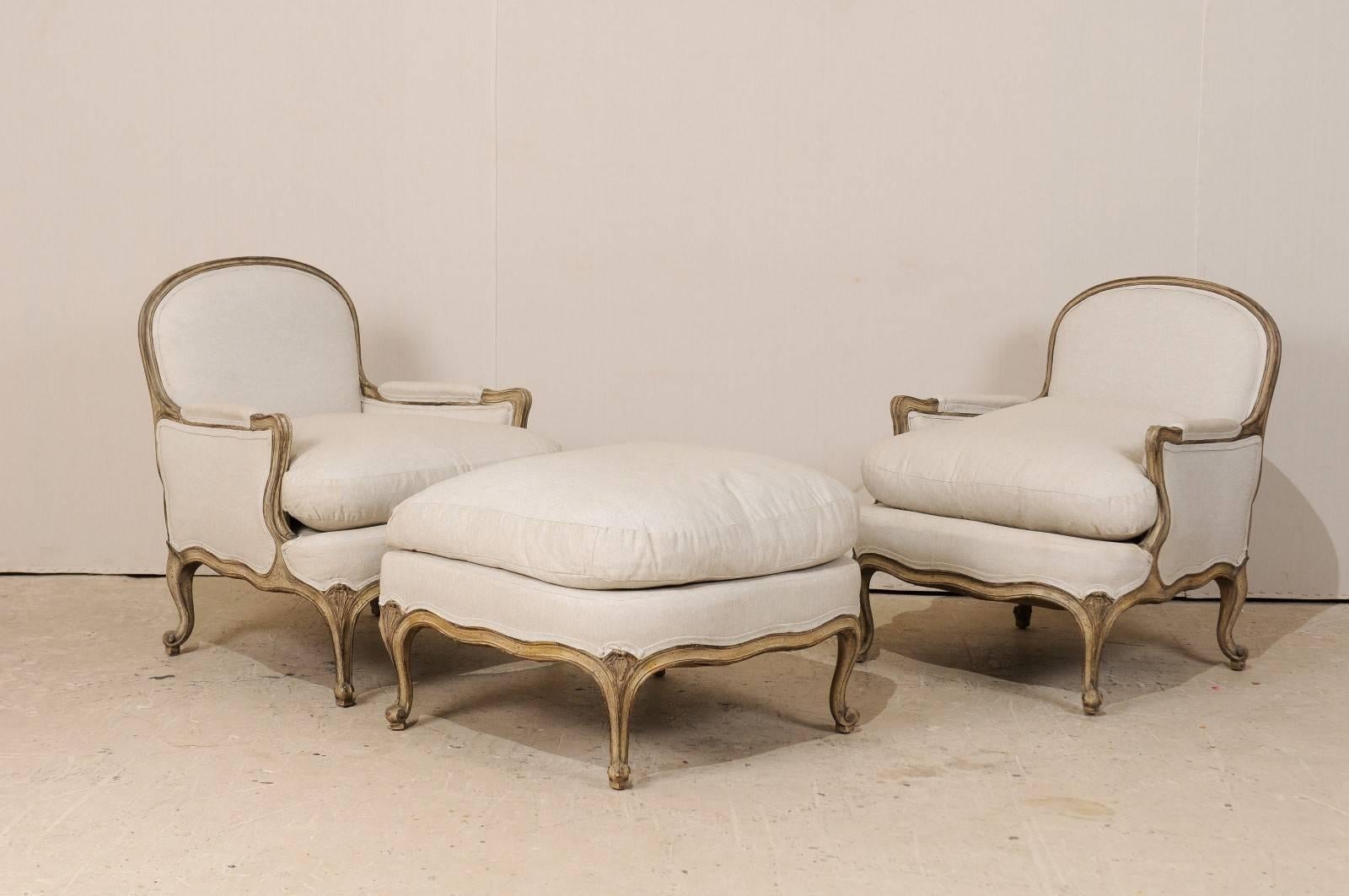 A set of two French vintage bergères chairs accompanied with their pouf (ottoman). This set of French chairs and ottoman from the 20th century, feature manchettes on arms, cabriole legs and oblate backs. The three-piece set have been newly