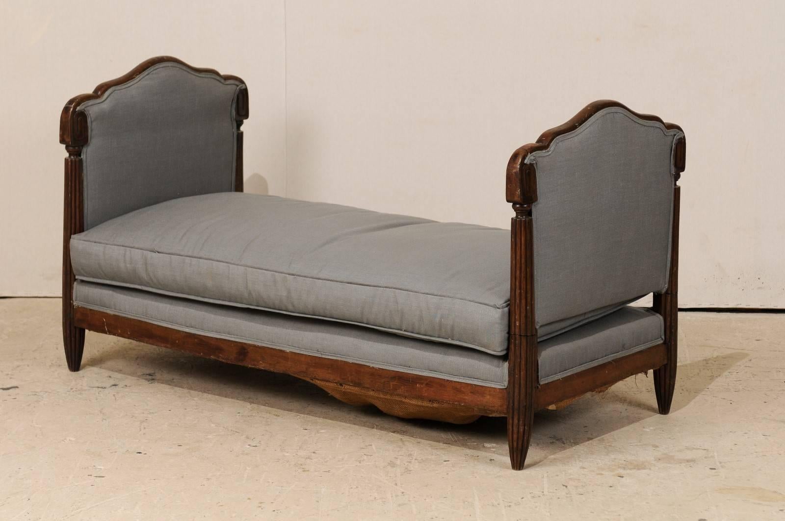 A French Deco style Lit de Jour (daybed). This French daybed, from the early 20th century, features a carved walnut frame with reeded legs. There is a drop arm which provides more extension for more versatility. This French Lit de Jour would be