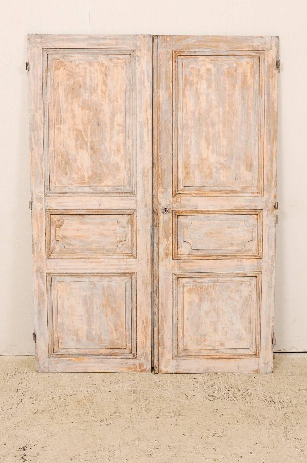Pair of European 19th French style doors. This pair of cute sized French style doors, from the 19th century have a blue or grey color with taupe accents and wood showing throughout. Each door has three raised panels that breaks up the surface and