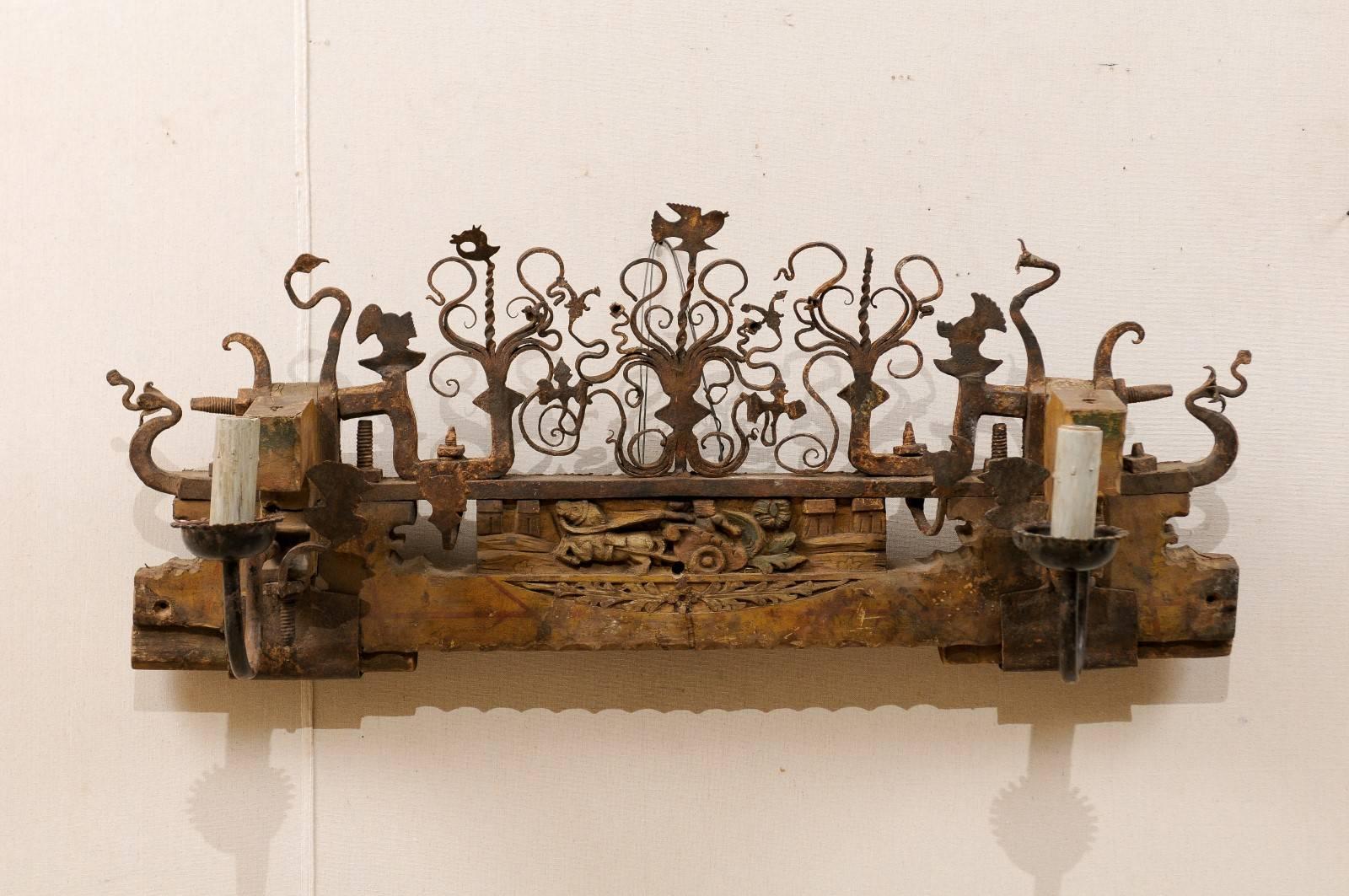 A single Sicilian two-light sconce of cut metal and wood. This unique Sicilian sconce, from the mid-20th century, is composed of a wood base with cut metal design, which was the original decorative piece from and ox cart. The sconce is adorn with