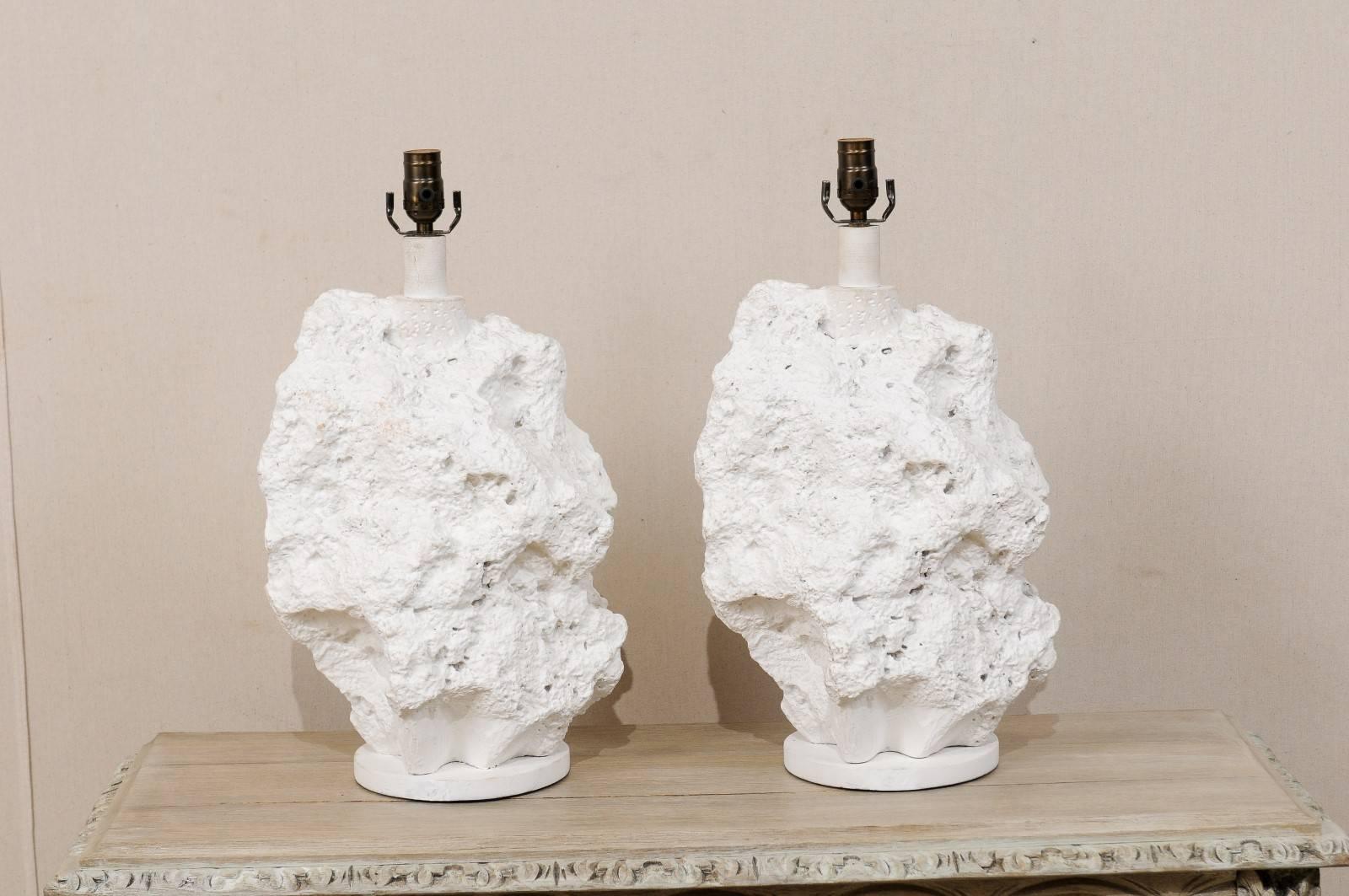 A pair of modern vintage American table lamps attributed to Sirmos. This pair of American table lamps feature a modern, rock like design. The lamp bodies are made of plaster, rest on a round wood base and are white in color. The height of the lamps