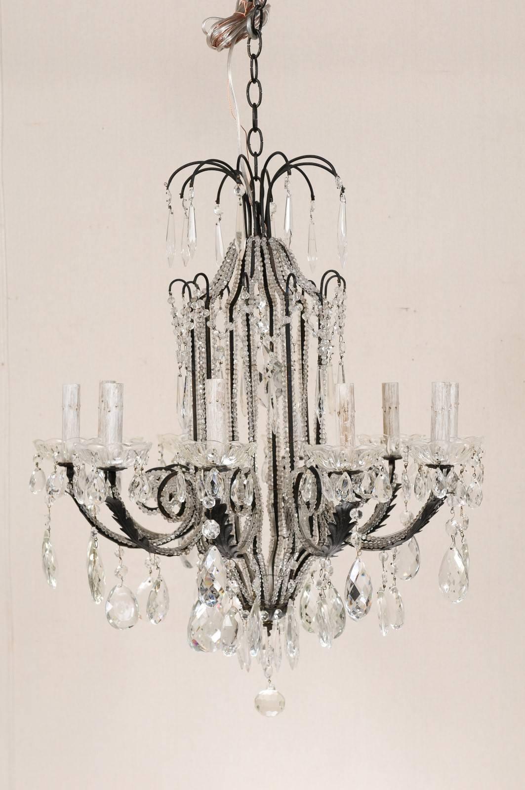 An Italian ten-light crystal and wrought iron chandelier. This Italian mid-20th century chandelier of black wrought iron is outlined along the body and arms with Italian bead-like glass trim. There is a crystal waterfall crown and hanging finial at
