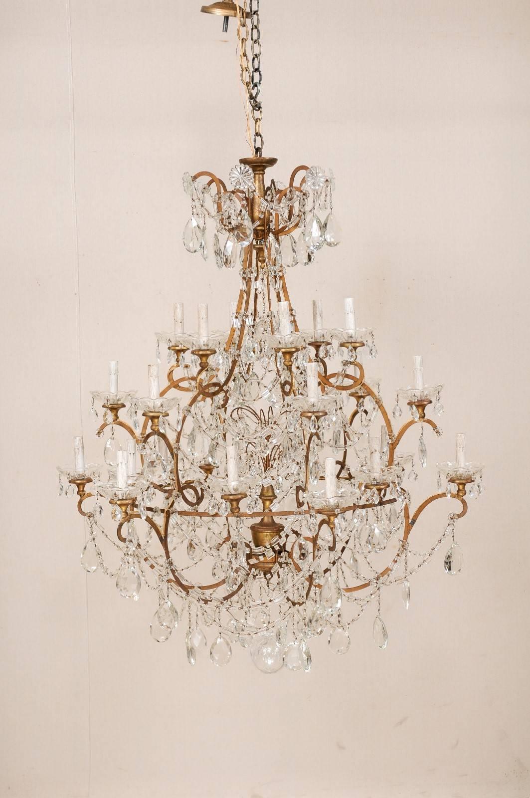 An Italian grand scale three-tier crystal chandelier. This Mid-Century Italian chandelier features an awe-inspiring twenty-four-lights displayed over three-tiers. The top is adorned with a crystal waterfall crown, with a series of flower shaped