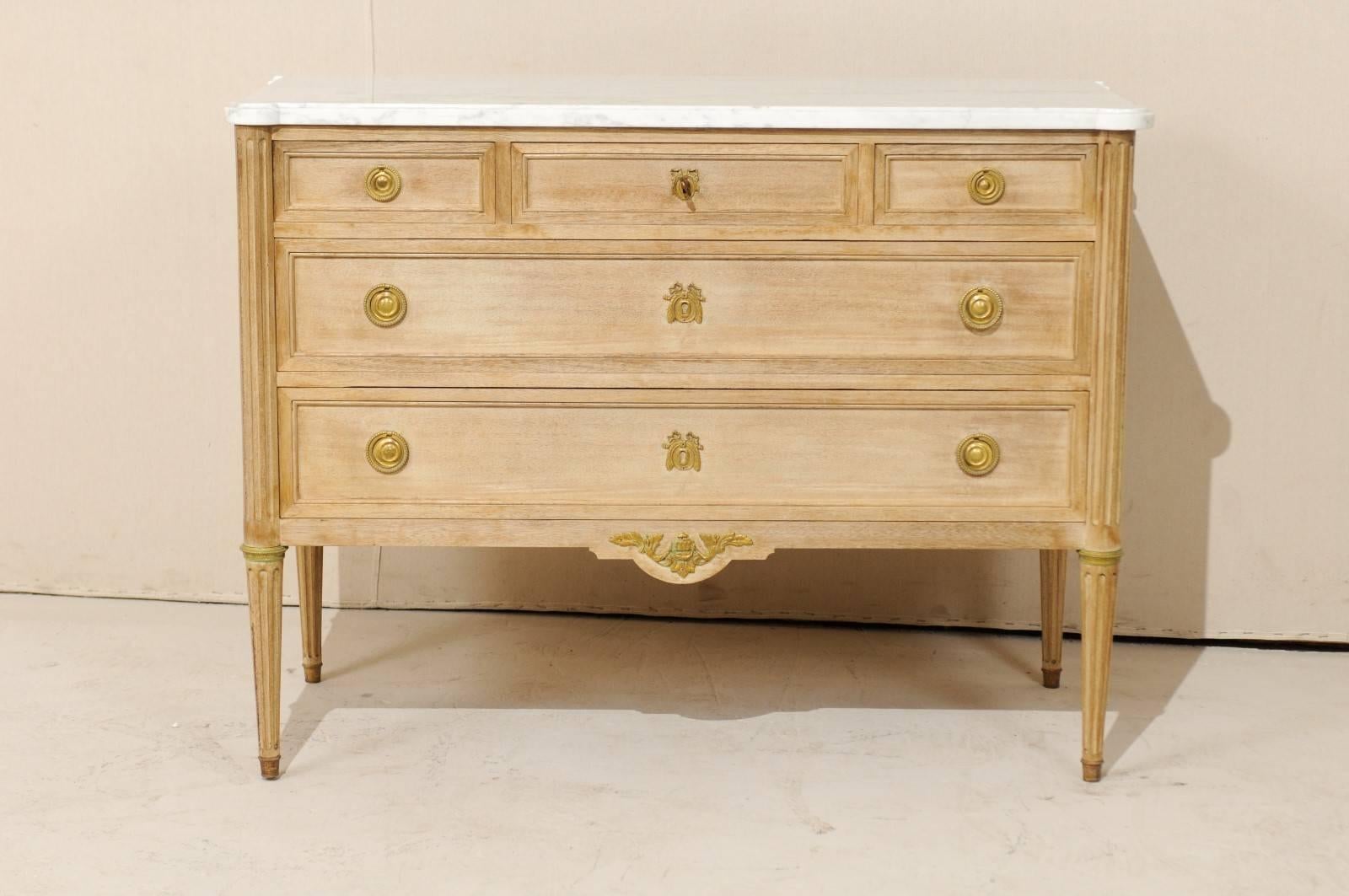 A French marble-top chest. This French chest of bleached mahogany from the mid-20th century features three small top drawers over two larger drawers and a white marble top with gray veining. The marble top is slightly overhung and has protruded