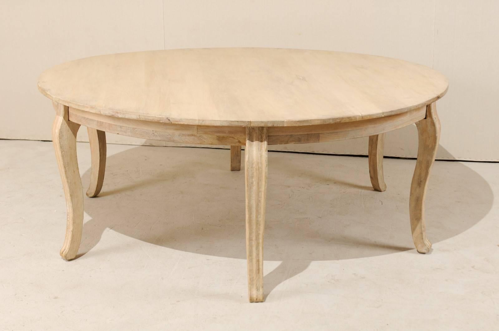 An American round wood dining table of grand size. This round-shaped American table, from the late 20th century, is raised on fluted, cabriole legs. The table is a bleached wood with a clear matte coat. The table is accented with a pale cream